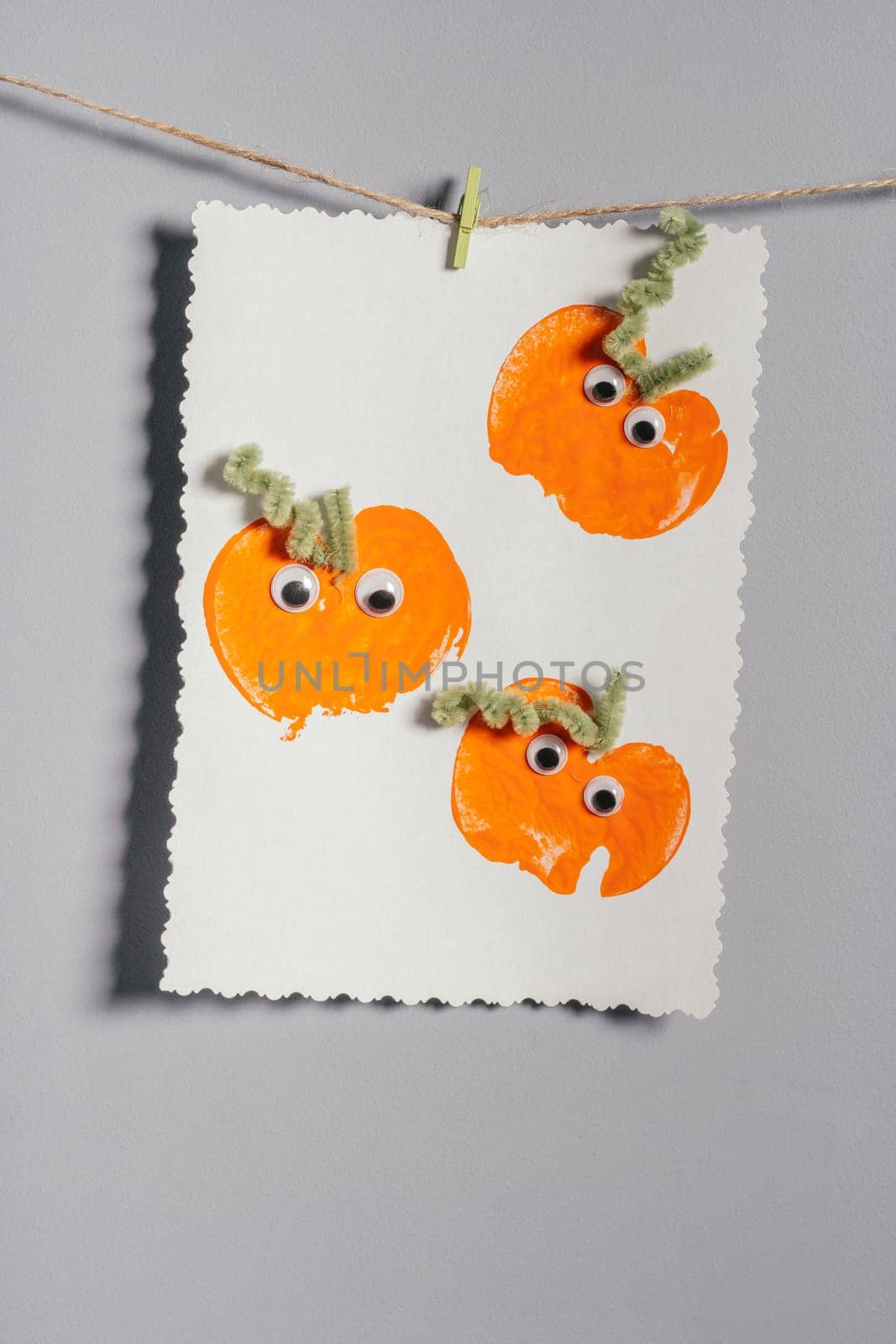 Halloween childrens pumpkin apple prints drawing hanging on rope on gray wall. Handmade DIY decoration with children for holiday. Vertical
