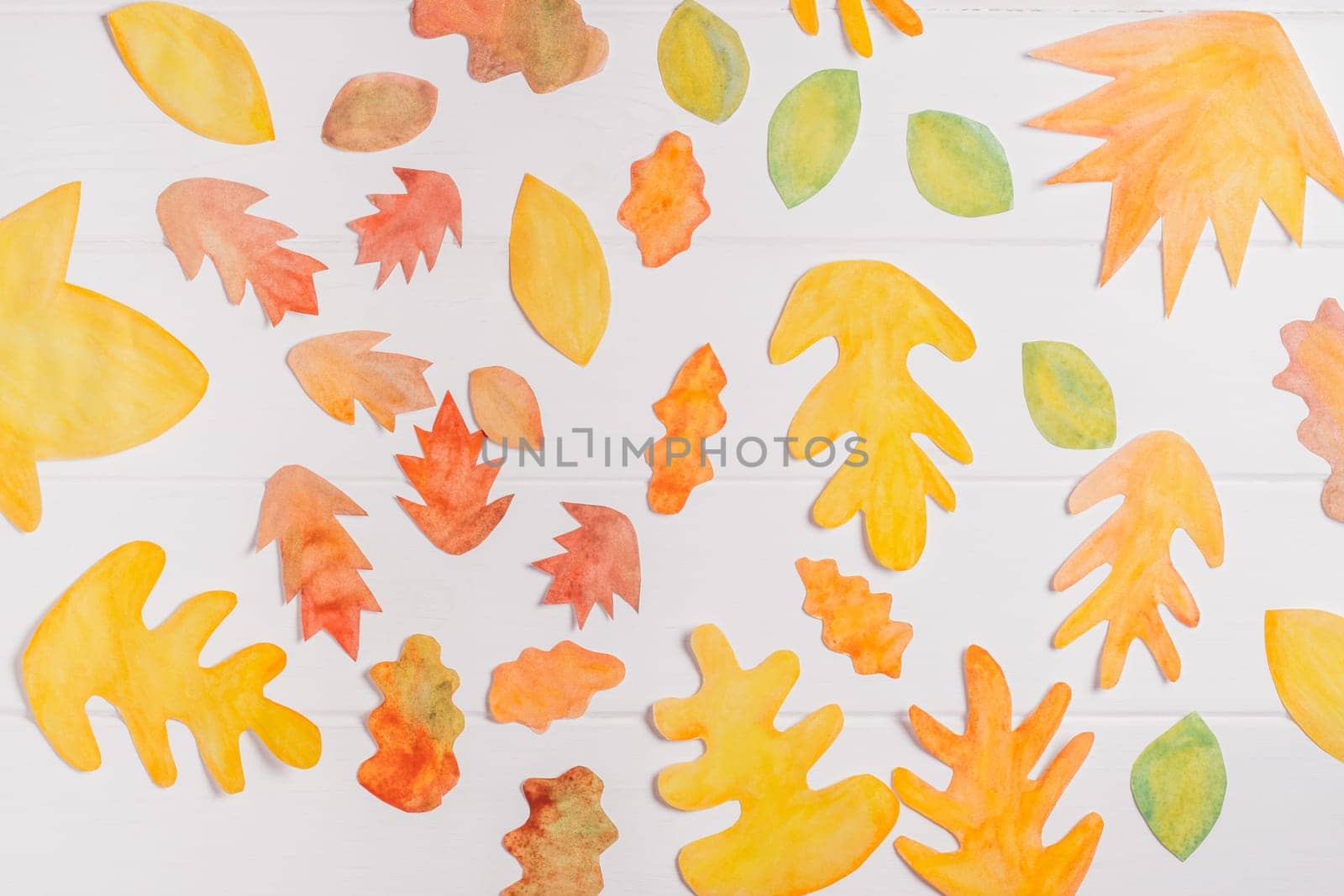 Background image of cut paper red, orange and yellow autumn leaves painted in watercolor laid out on white wooden planks. top view. DIY handmade autumn decorations