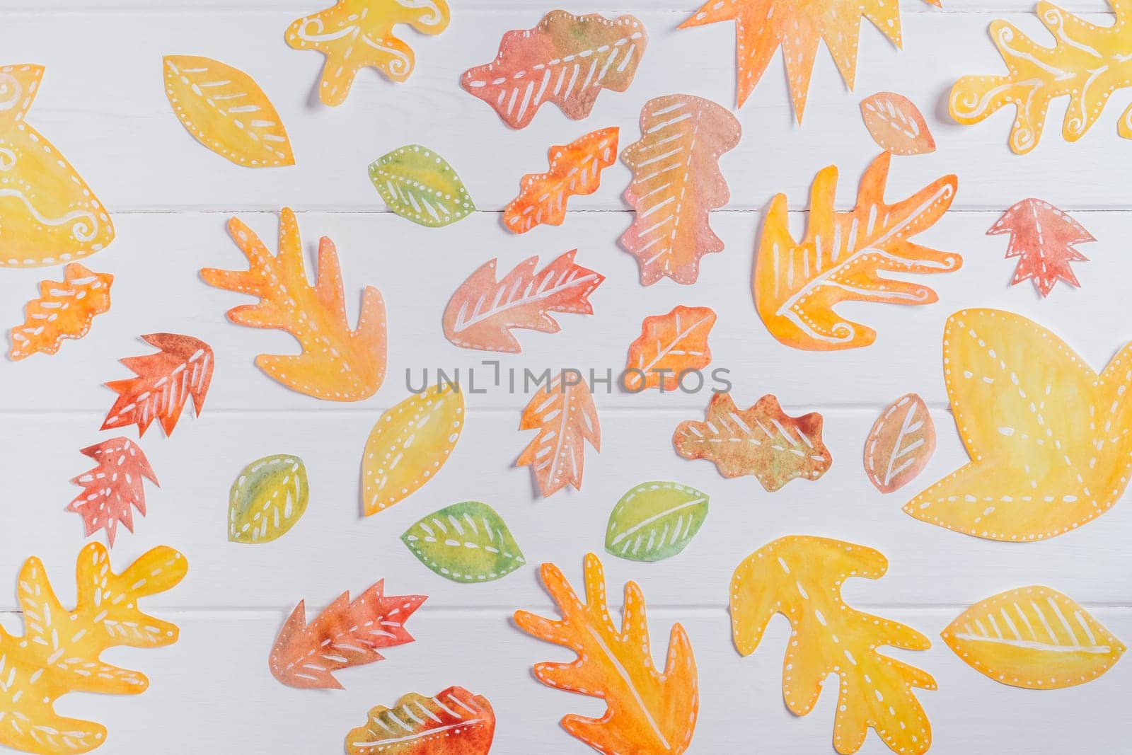 Background image of cut paper red, orange and yellow autumn leaves painted in watercolor laid out on white wooden planks. top view. DIY handmade autumn decorations