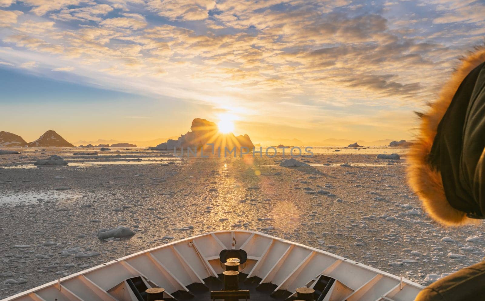 Cruise ship sails through wintry Cierva Cove - a deep inlet on the west side of the Antarctic Peninsula, ringed by Cierva Bay in San Martín Land - Antarctica, during a dramatic sunset / evening sunset.