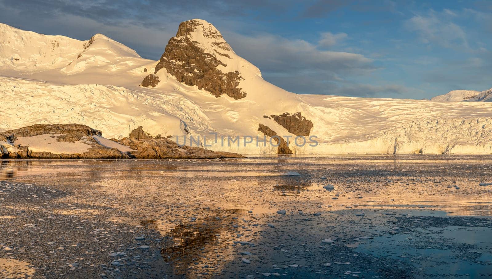 Cruise ship sails through wintry Cierva Cove - a deep inlet on the west side of the Antarctic Peninsula, ringed by Cierva Bay in San Martín Land - Antarctica, during a dramatic sunset / evening sunset.