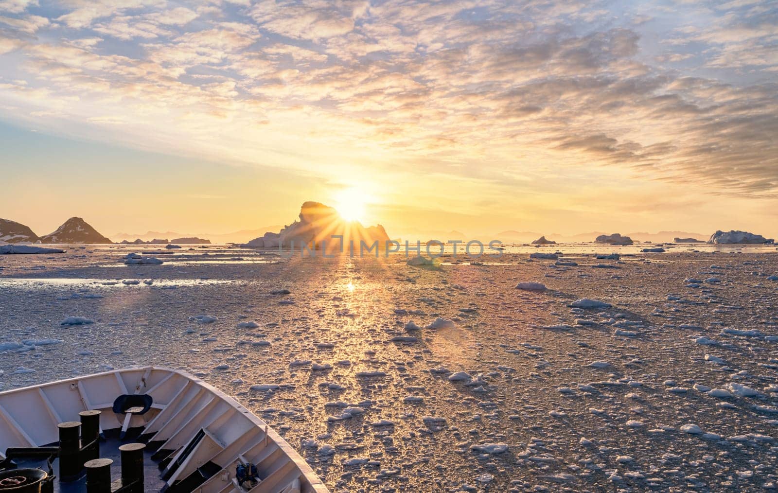 Cruise ship sails through wintry Cierva Cove - a deep inlet on the west side of the Antarctic Peninsula, ringed by Cierva Bay in San Martín Land - Antarctica, during a dramatic sunset / evening sunset.