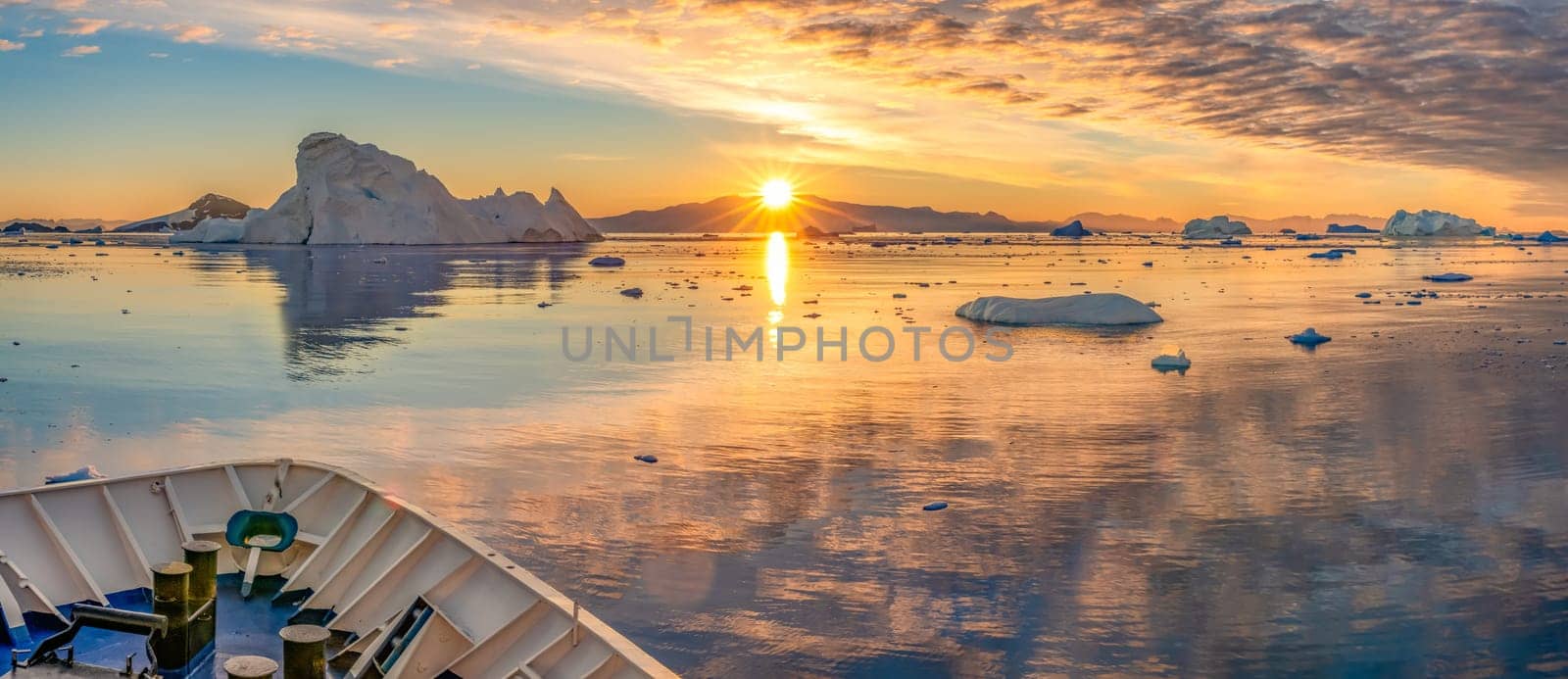 Cruise ship sails through wintry Cierva Cove - a deep inlet on the west side of the Antarctic Peninsula, ringed by Cierva Bay in San Martín Land - Antarctica, during a dramatic sunset / evening sunset.