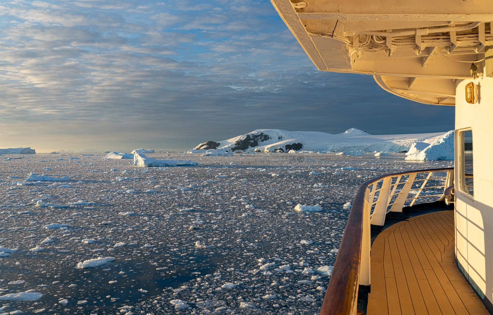 Cruise ship sails through wintry Cierva Cove - a deep inlet on the west side of the Antarctic Peninsula, ringed by Cierva Bay in San Martín Land - Antarctica, during a dramatic sunset / evening sunset.
