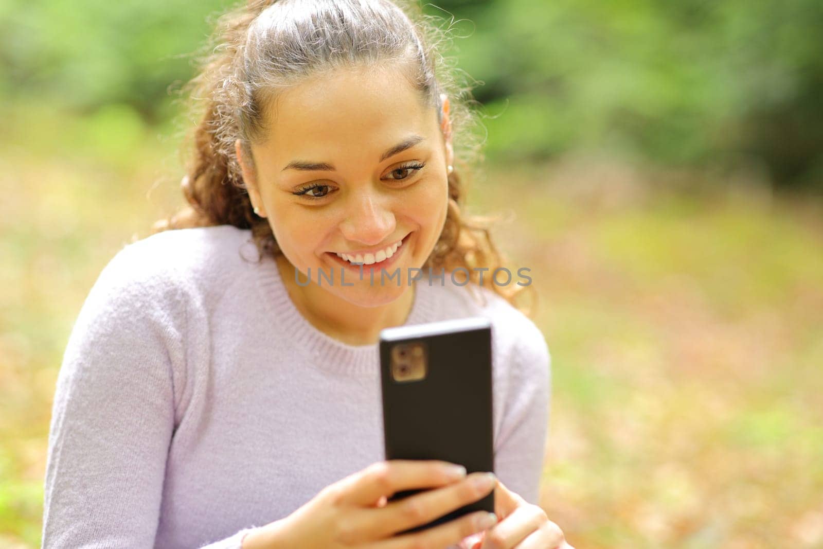 Happy woman sitting in a forest or park using smart phone