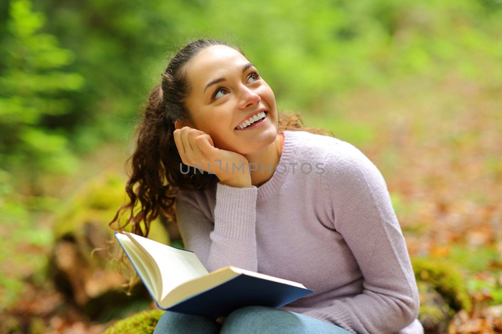 Happy woman dreaming while read a book in a forest looking above
