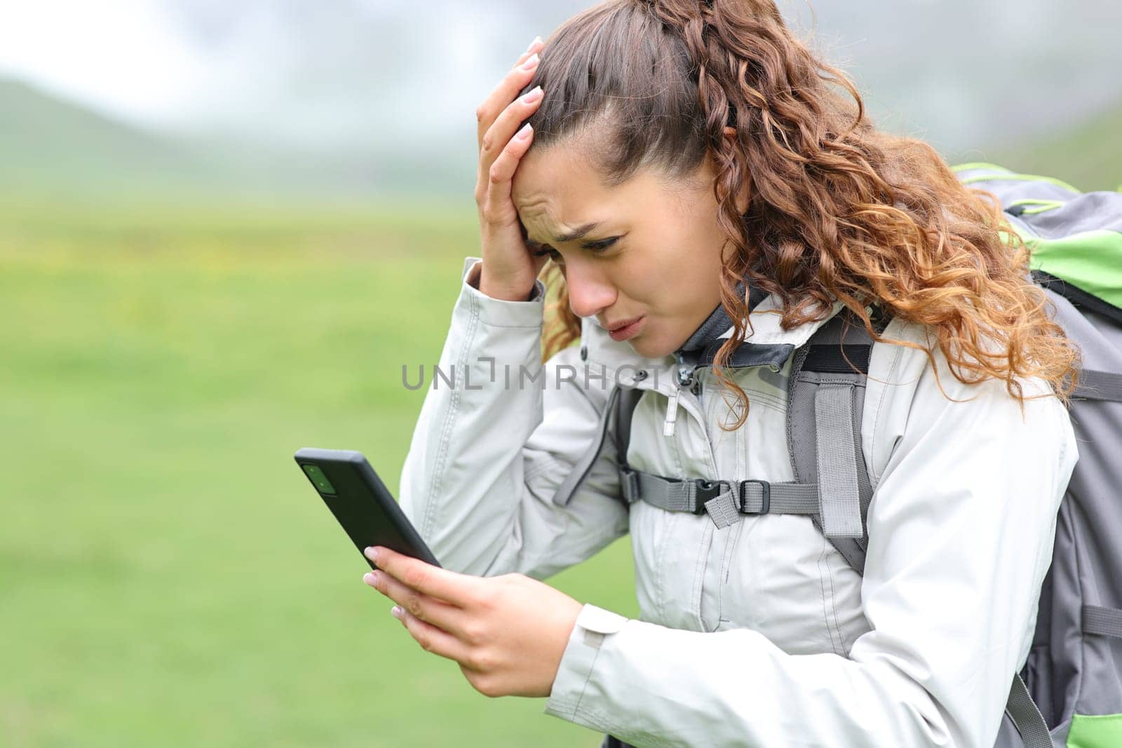 Worried hiker checking smart phone news or gps location in the mountain