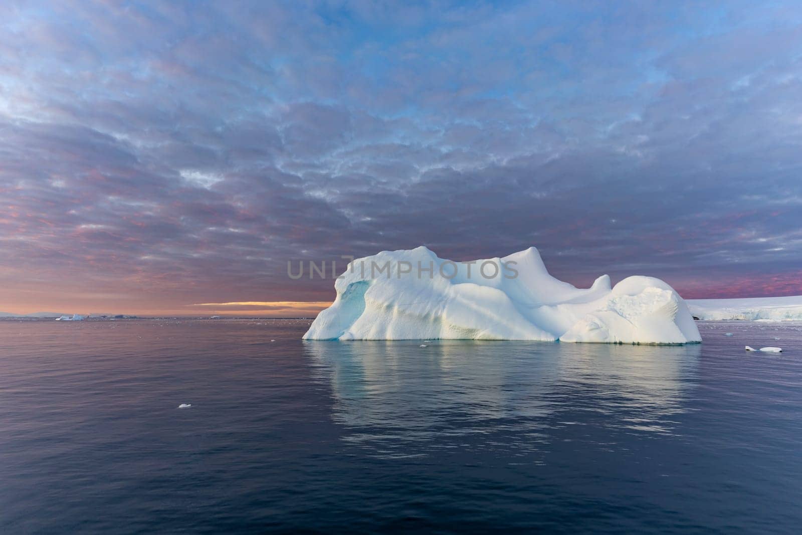 Cruise ship sails through wintry Cierva Cove - a deep inlet on the west side of the Antarctic Peninsula, ringed by Cierva Bay in San Martín Land - Antarctica, during a dramatic sunset / evening sunset.