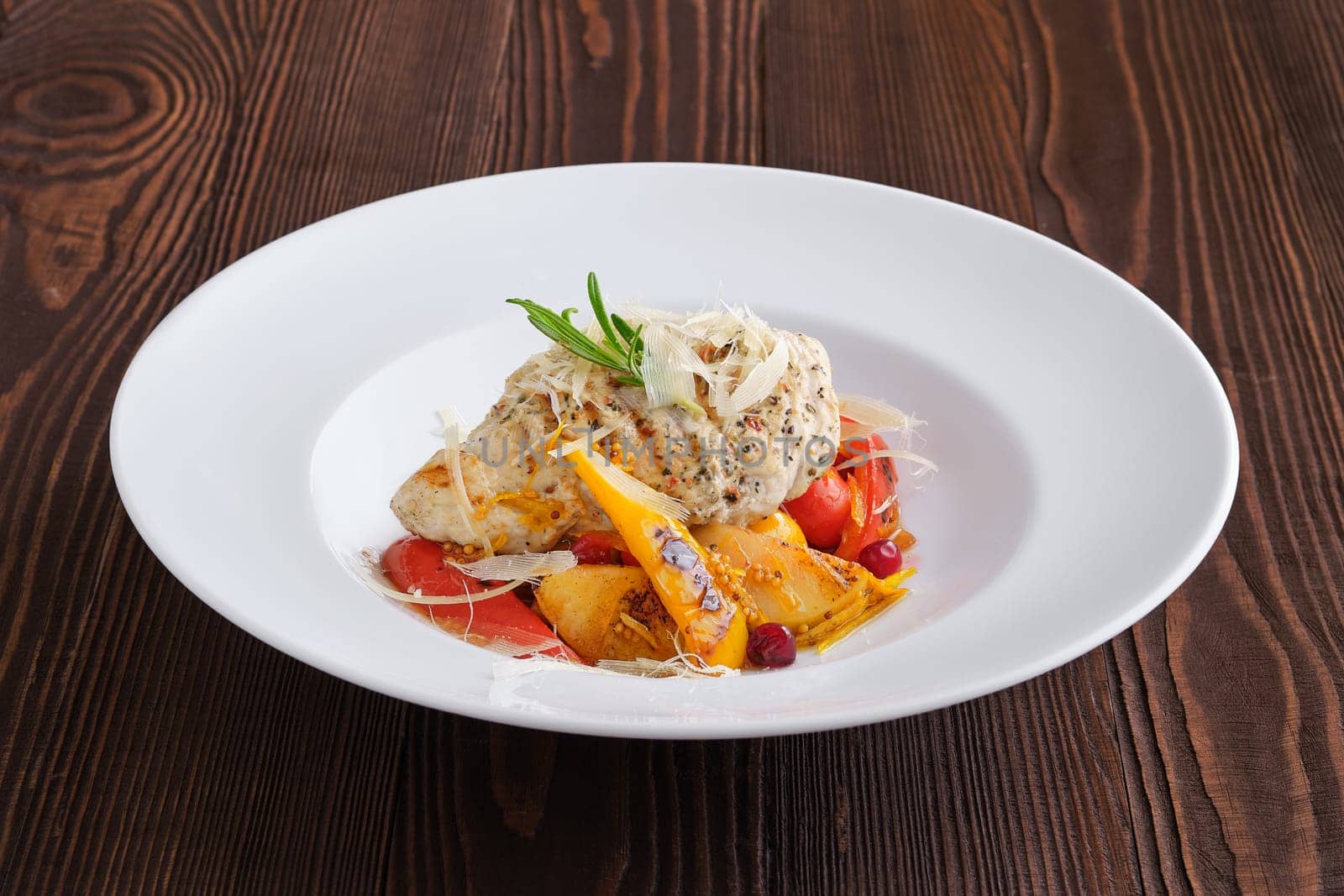 Fried turkey meat with roasted tomato and bell pepper served with parmesan, cranberry and orange balsamic sauce on dark wooden background
