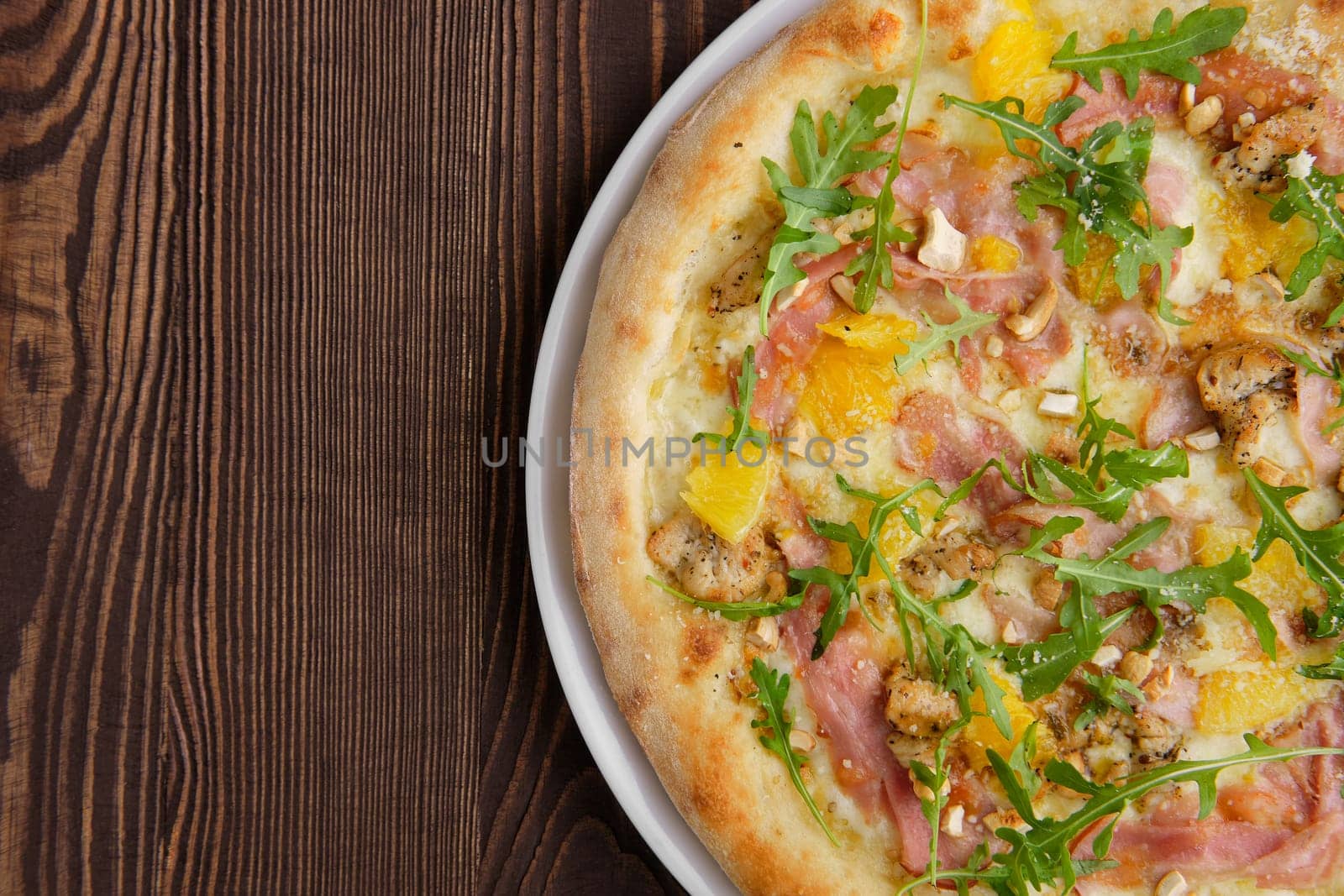 Pizza with turkey, bacon, orange and cashew nuts on dark wooden background