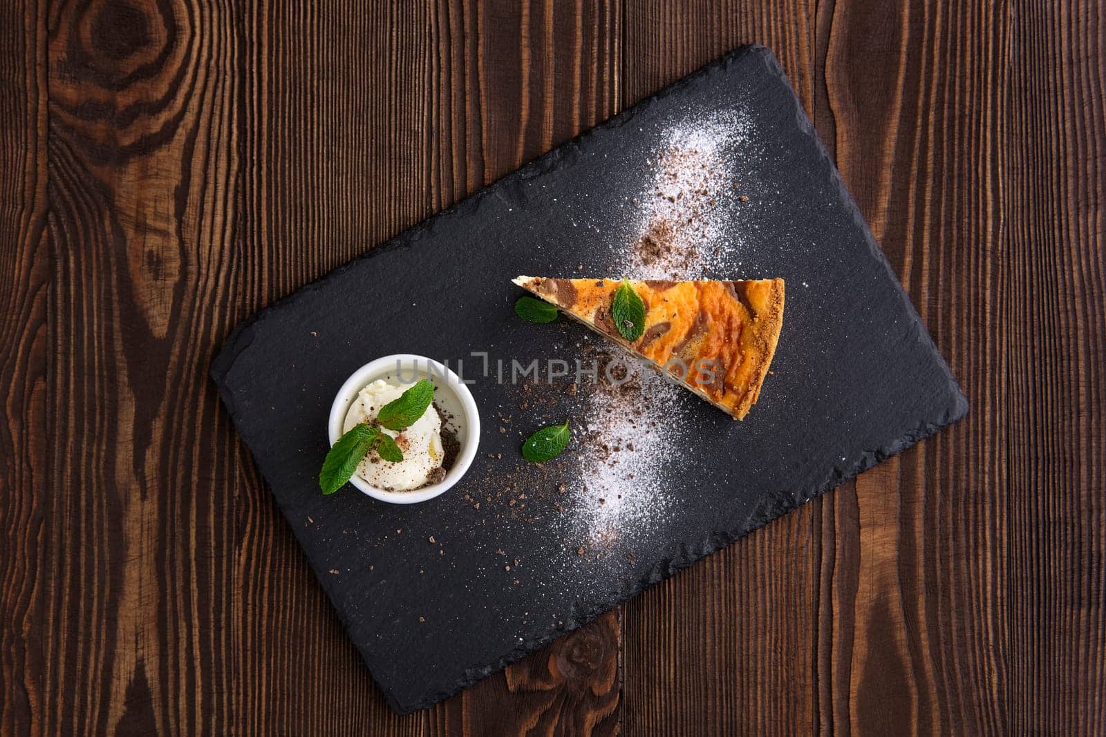 Top view of layered cheesecake with ice cream served on slate plate on dark wooden background