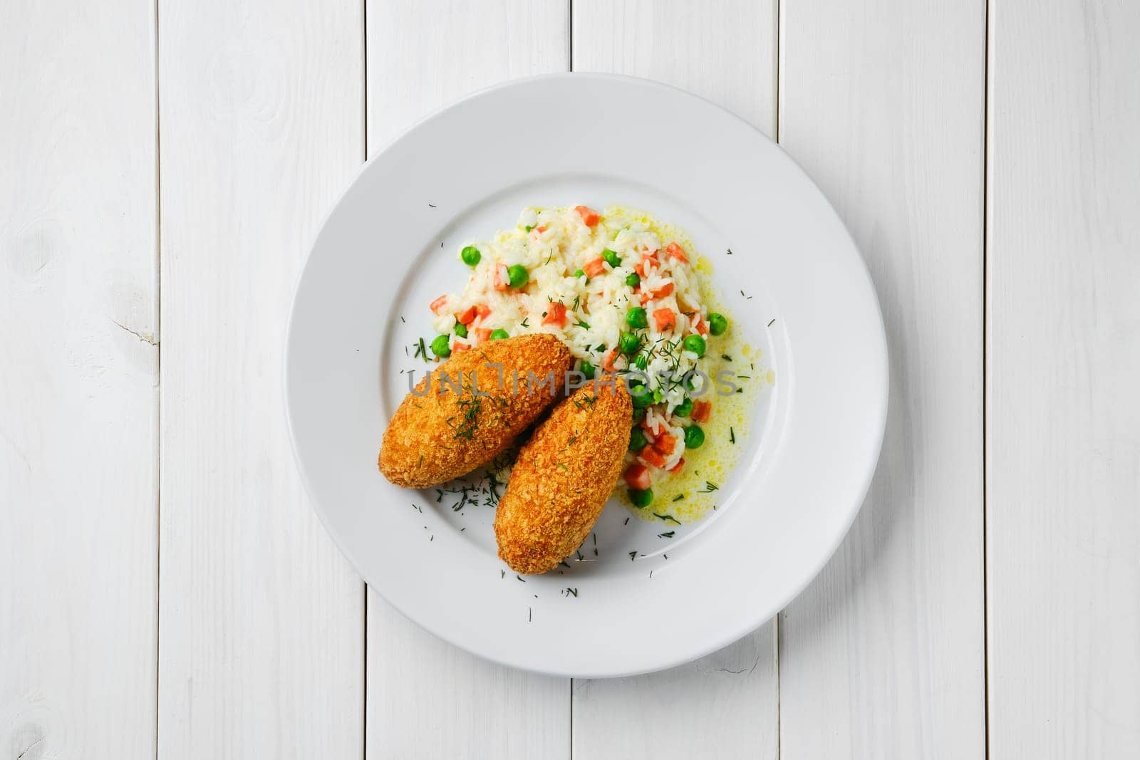 Top view of cutlet stuffed with cheese served with rice, green pea and carrot on white wooden table