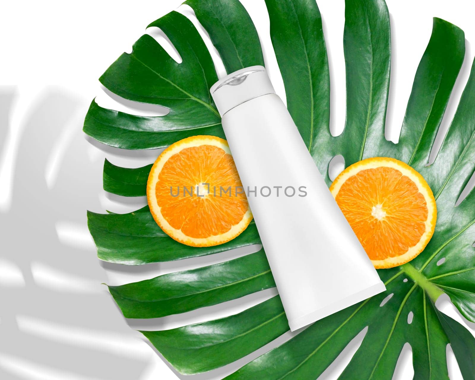 Luxury skin care product ad, top view of blank packaging cosmetic plastic tube with monstera leaf and oranges