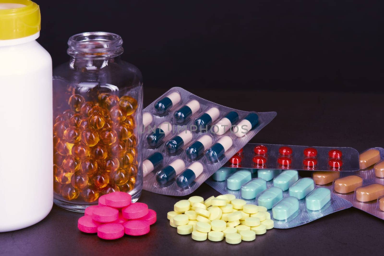 Pills and tablets of different colors are scattered and in bottles on a dark background