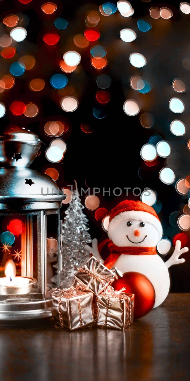 Christmas composition: A snowman, a lantern with candles, bright shiny boxes with gifts, blurred bokeh lights in the background.