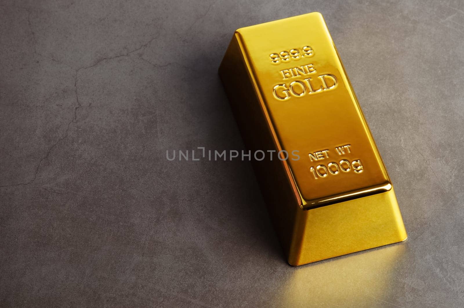 An ingot of gold metal bullion of pure brilliant diagonally located on a gray textured background