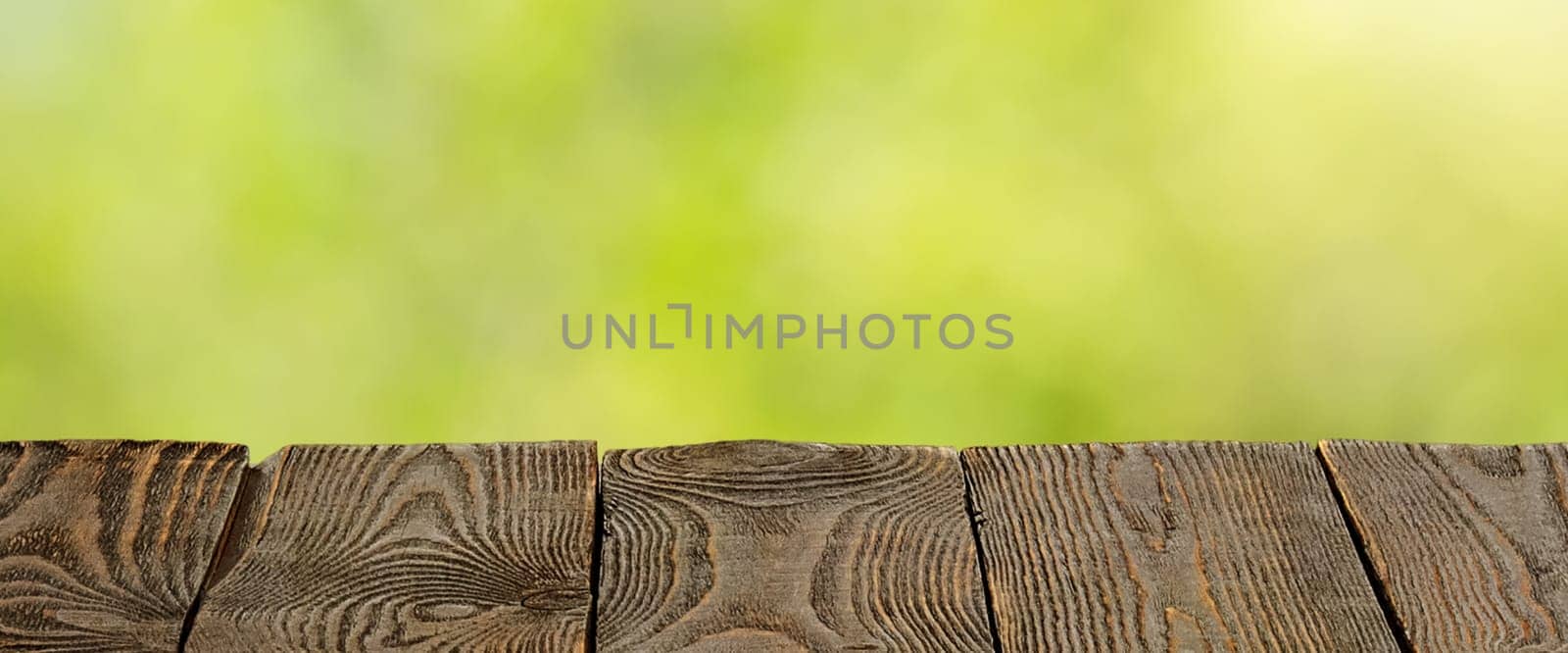 Background with blurred green leaves and empty wooden planks in the foreground. For product demonstrations, free space, layout, mockup, perspective board, background board.