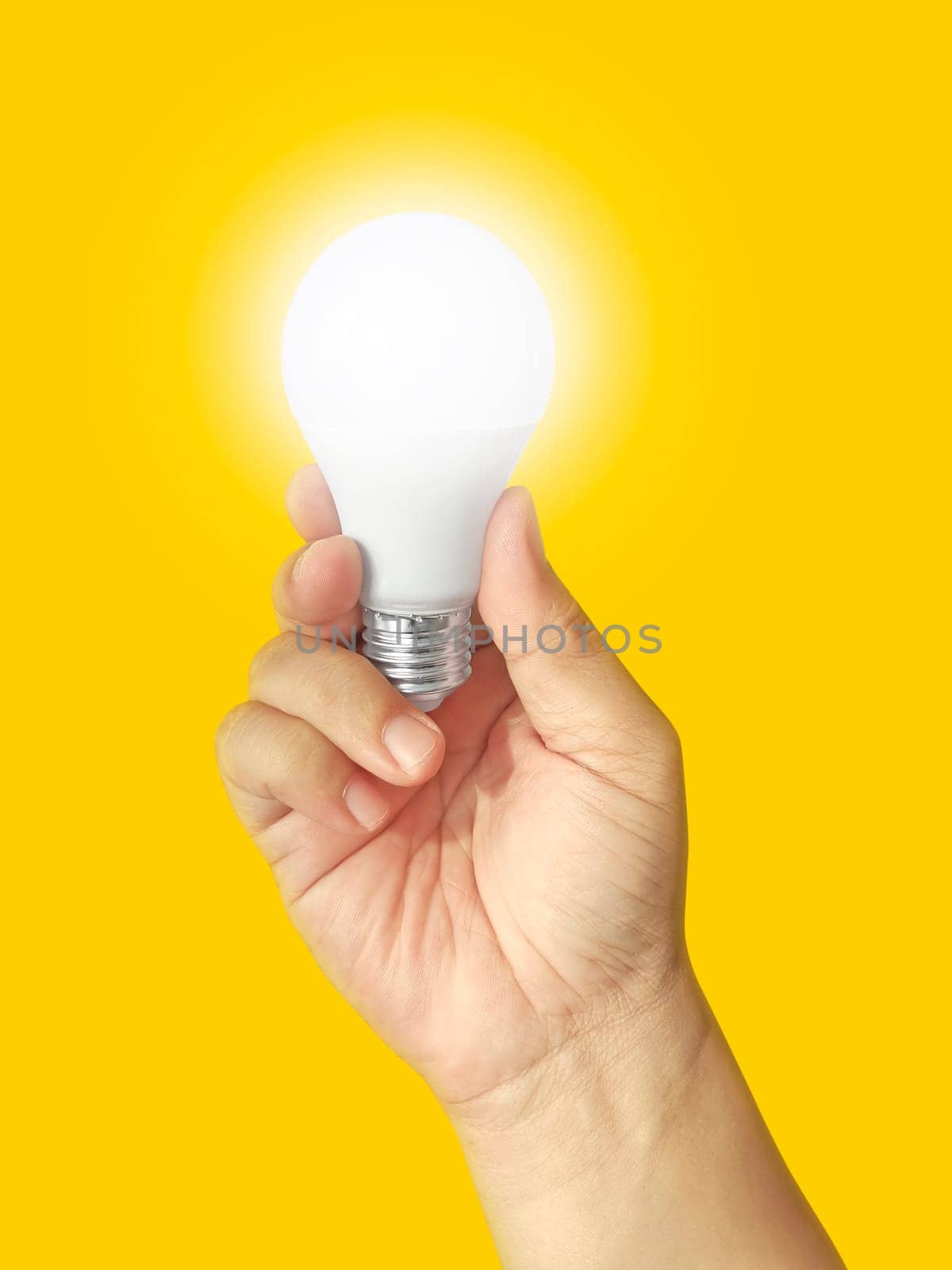 Human hand holding light bulb illuminated on yellow background. Creativity, inspiration, flat lay design idea