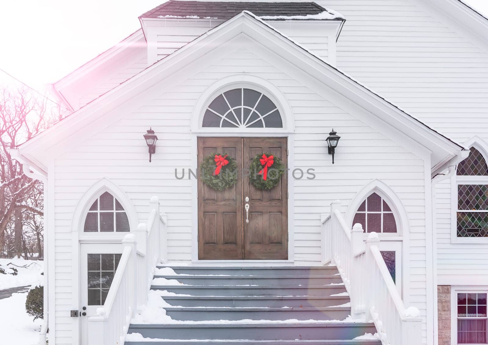 Christmas Wreaths Hang from Entrance Doors of Rustic Church In Winter Snow Scene.