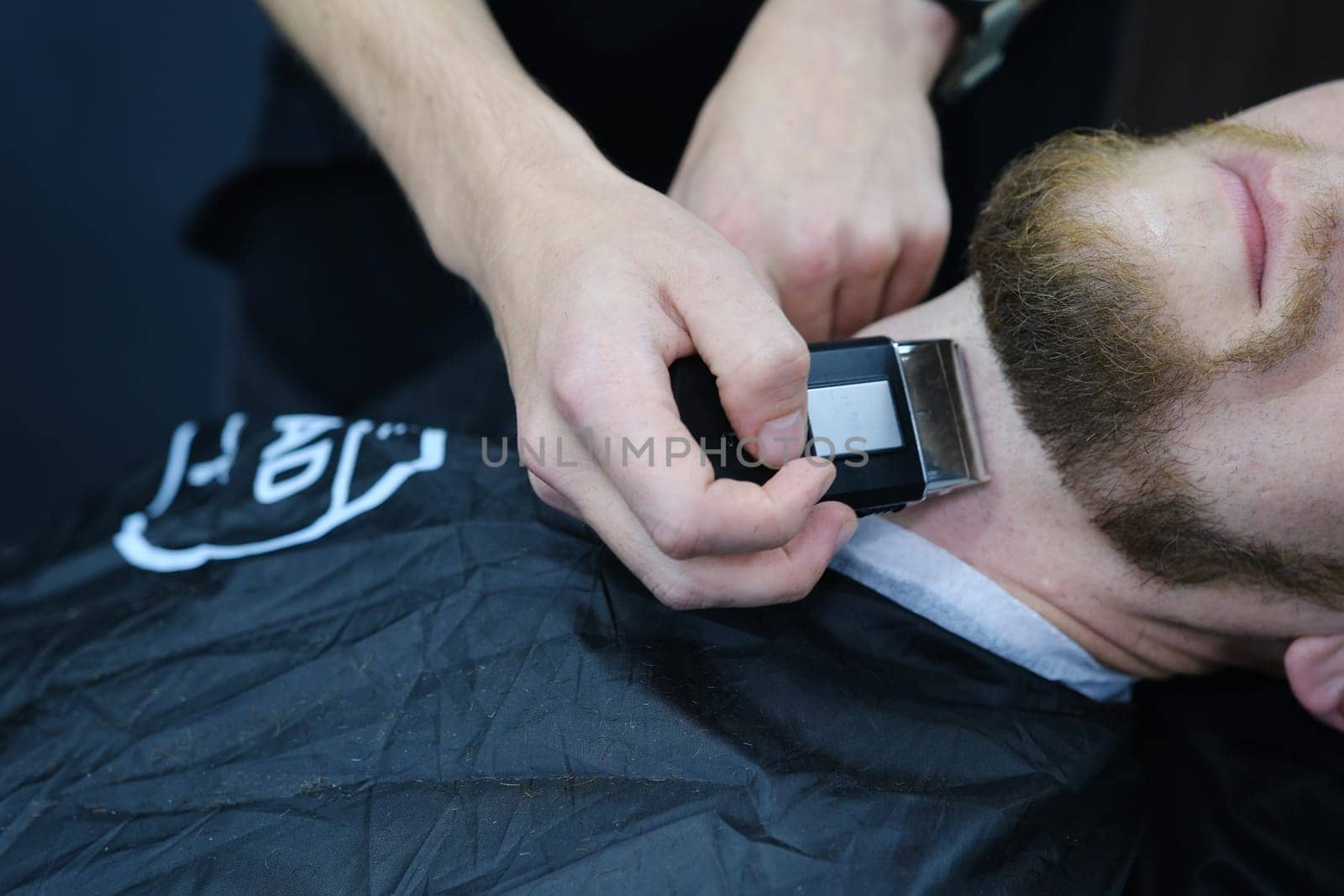 Professional Master barber shaves the client's beard with a electric trimmer. Haircut of a man's beard in a barber shop. Barber Men. Advertising and barber shop concept.