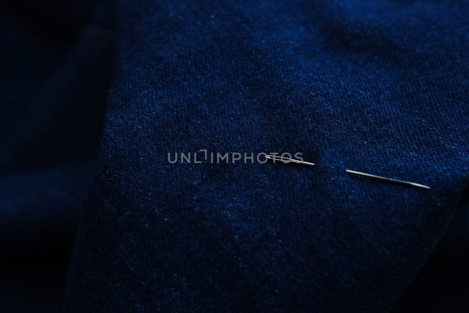 Sewing thread and needle at jeans denim background texture. Tailor handmade jeans denim concept.