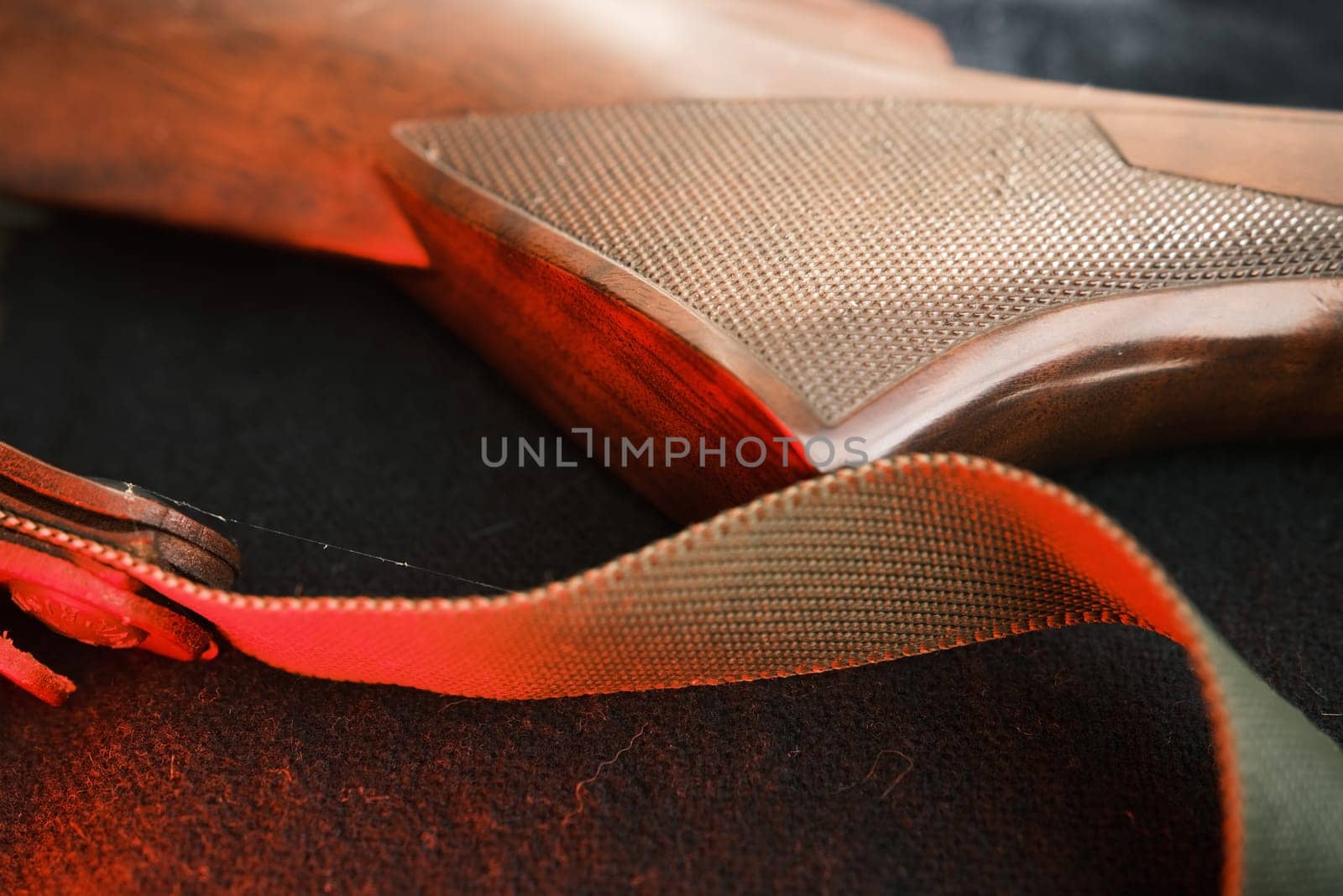 Closeup of a wooden shotgun butt. Hunting semi-automatic shotgun with a wooden button dark background with red light.