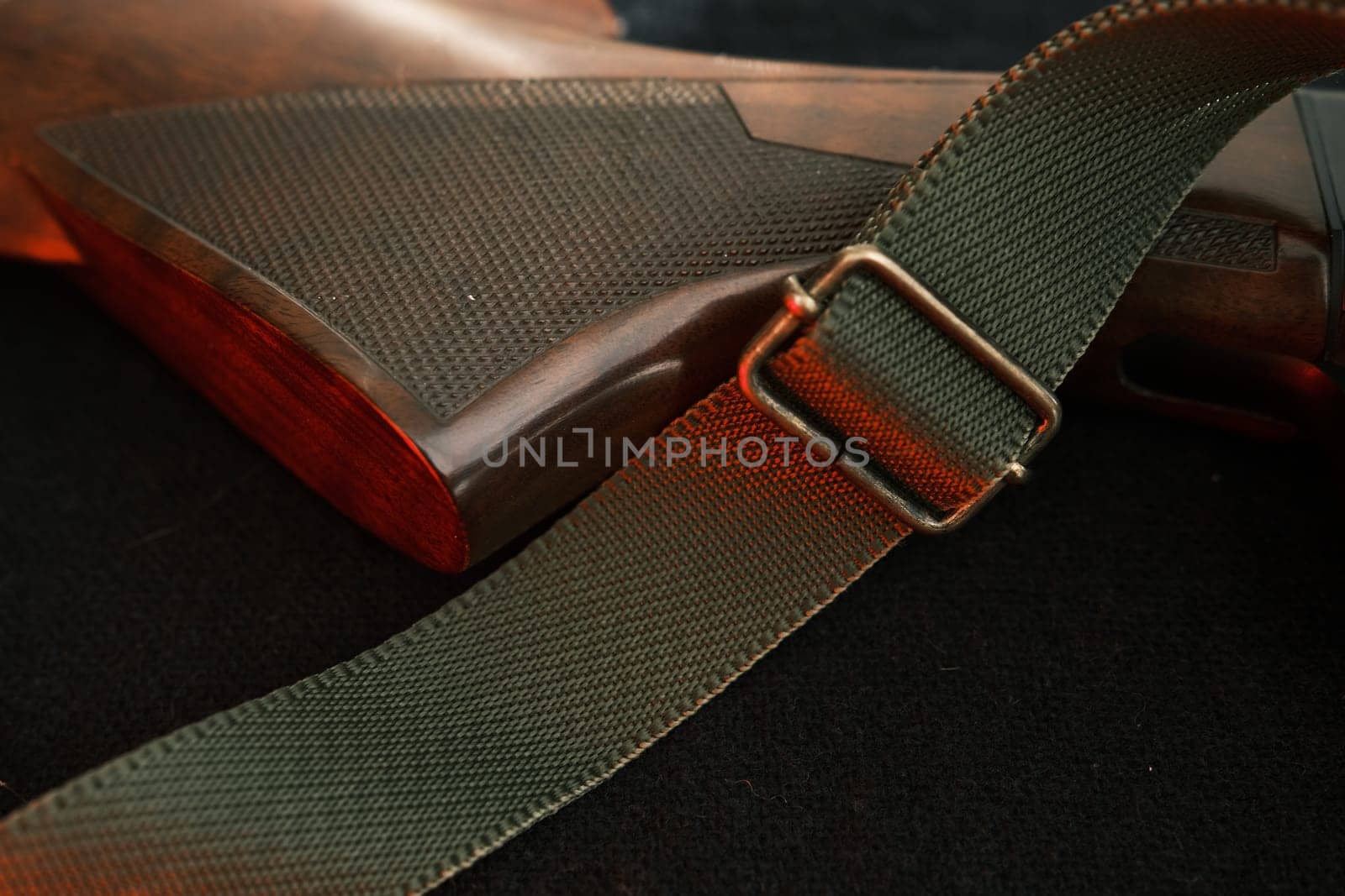 Closeup of a wooden shotgun butt. Hunting semi-automatic shotgun with a wooden button dark background with red light.