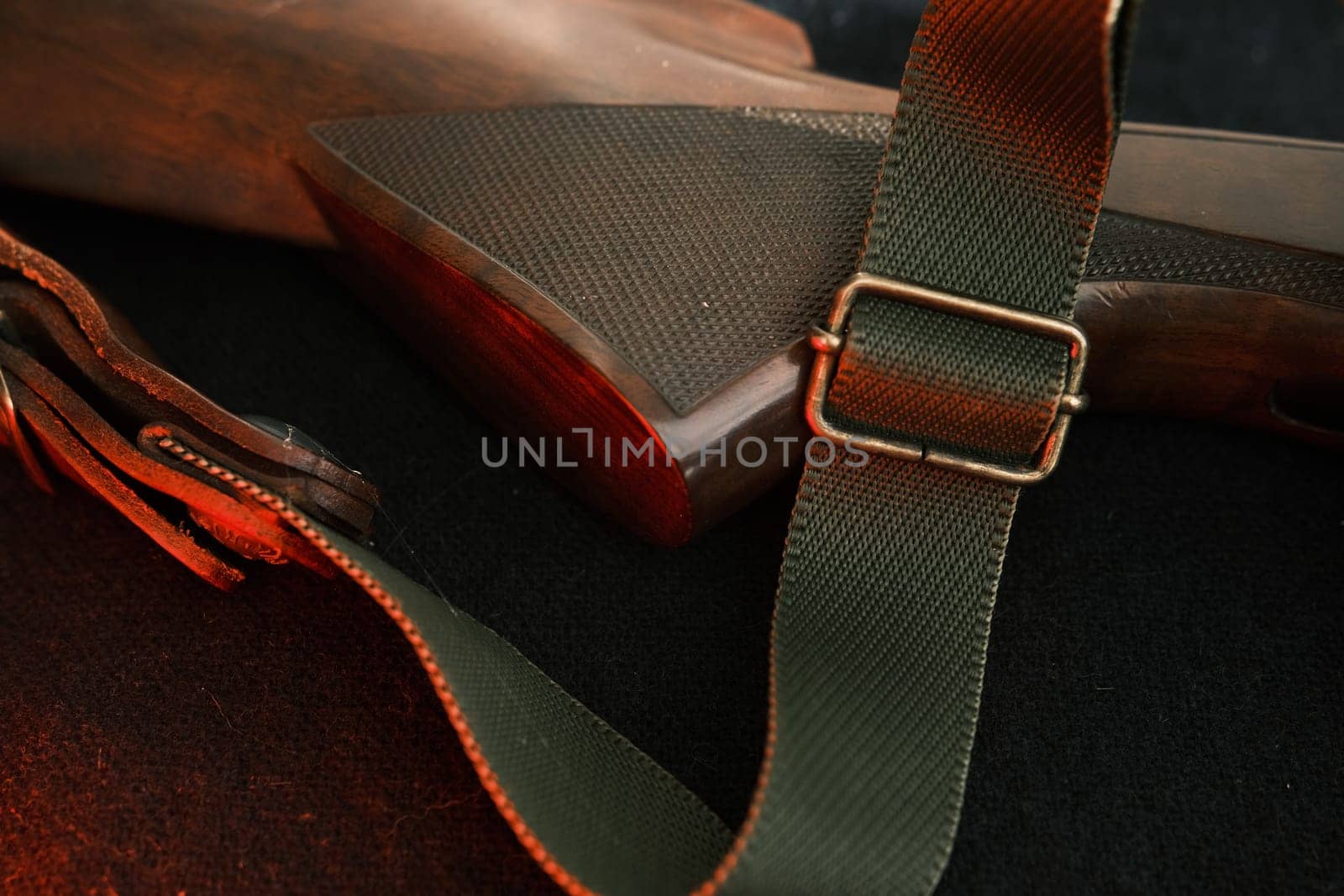 Closeup of a wooden shotgun butt. Hunting semi-automatic shotgun with a wooden button dark background with red light.