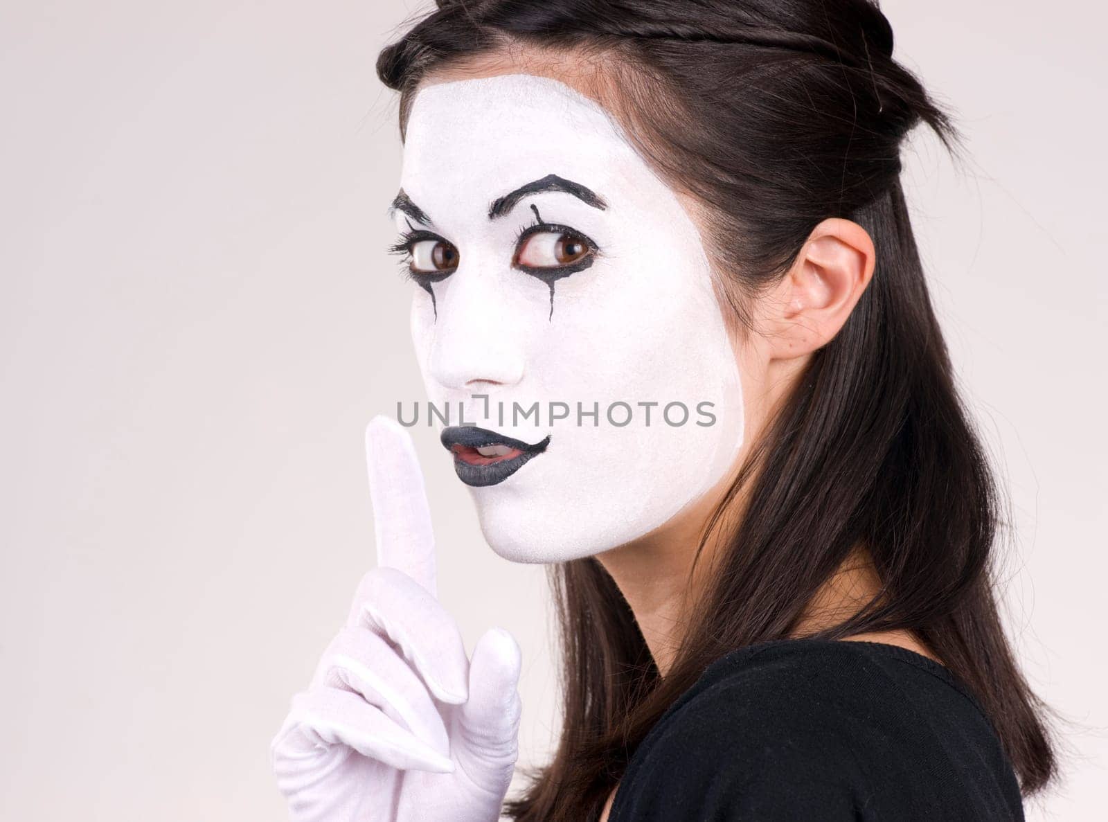 Woman made up in white face frames mouth with index finger