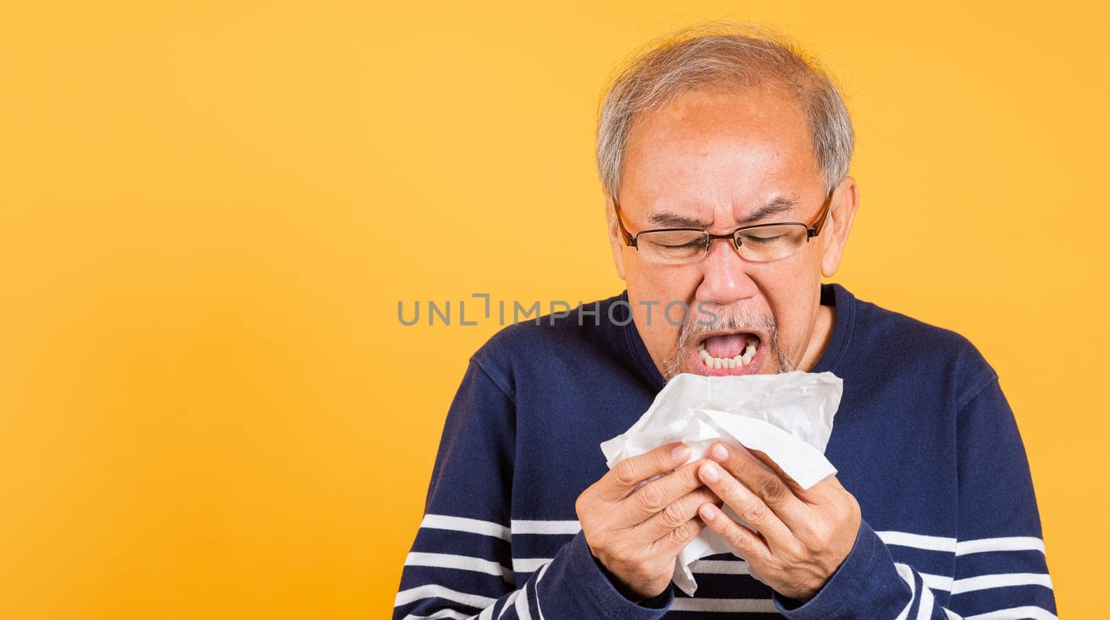 Asian elder man cold having flu and sneezing from sickness virus problem use tissue studio shot isolated on yellow background, Portrait senior old man blowing nose with tissue, pensioner unwell