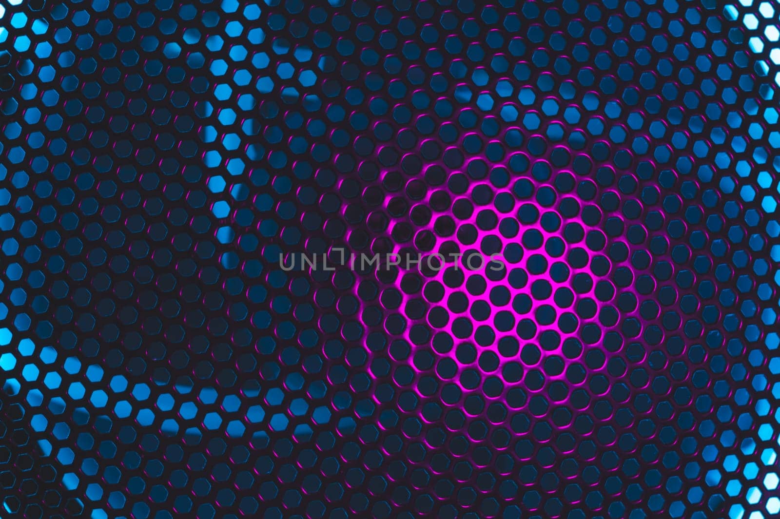 Colorful light of computer fan shines through the holes of protective grid. illumination glows in the dark. abstract futuristic background. led lighting of gaming pc
