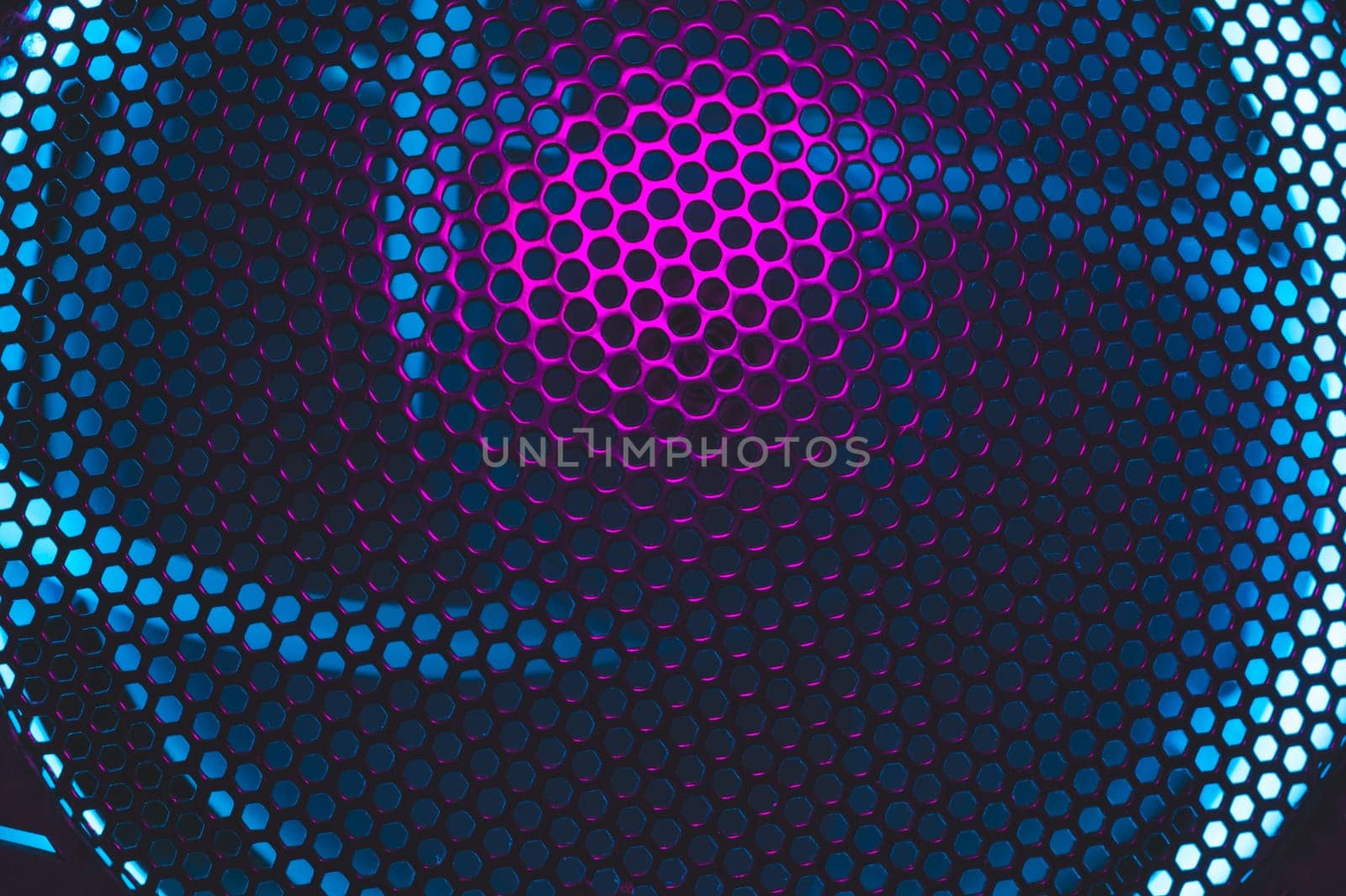 Colorful light of computer fan shines through the holes of protective grid. illumination glows in the dark. abstract futuristic background. led lighting of gaming pc