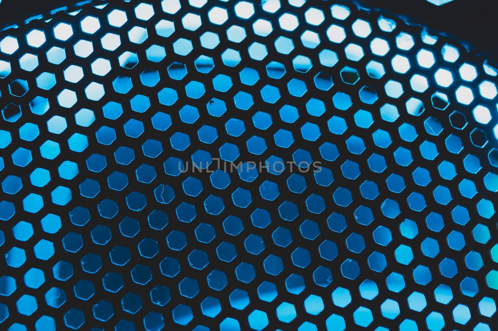 Blue light shines through the ventilation grid holes of computer air cooling system. abstract background