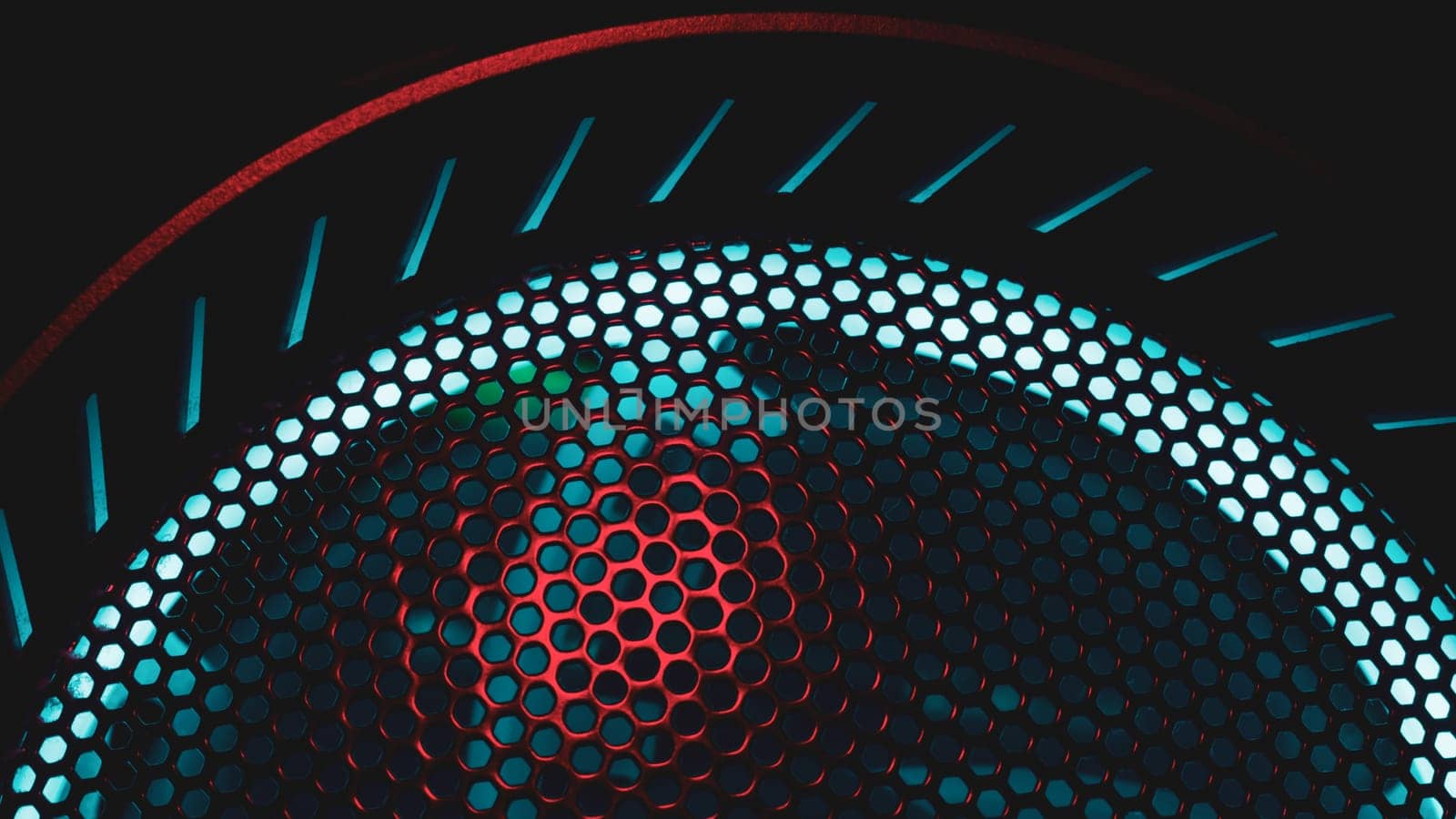 Colorful light of computer fan shines through the holes of protective grid. illumination glows in the dark. abstract futuristic background. led lighting of gaming pc