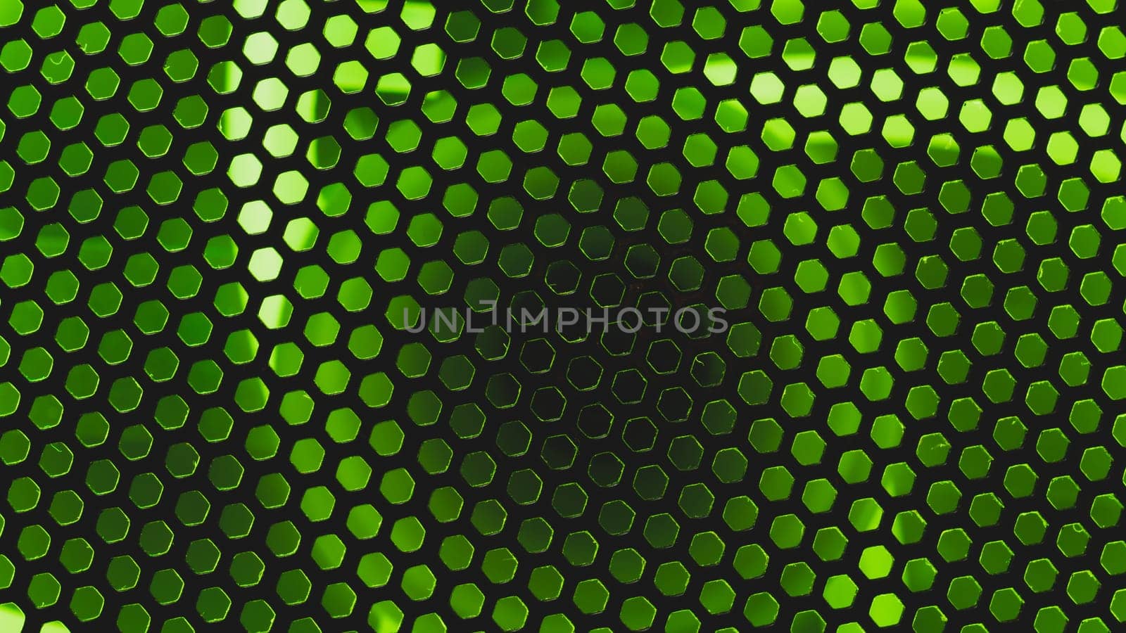 Green light shines through the ventilation grid holes of computer air cooling system. abstract background