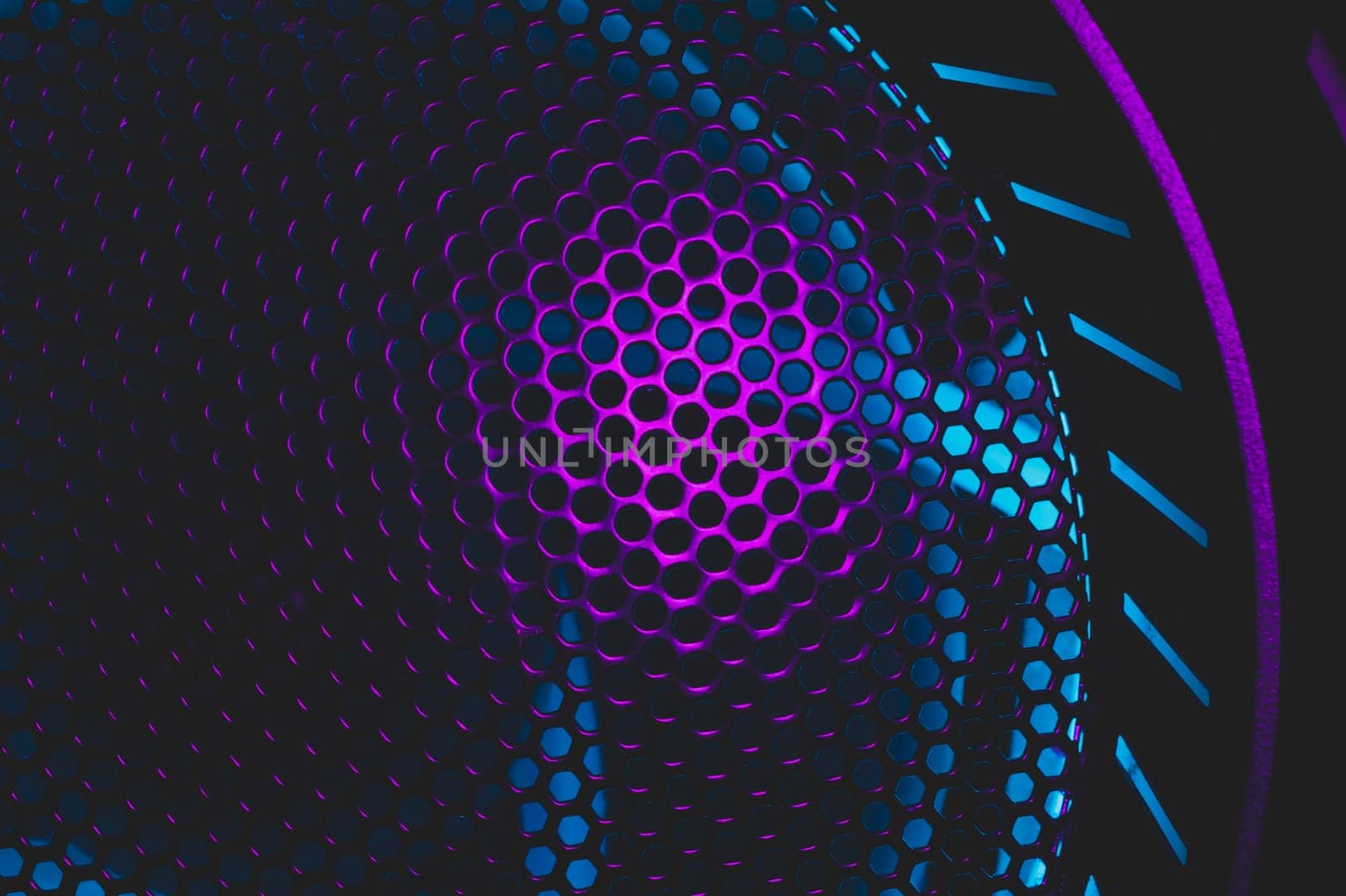 Colorful light of computer fan shines through the holes of protective grid. illumination glows in the dark. abstract futuristic background. led lighting of gaming pc