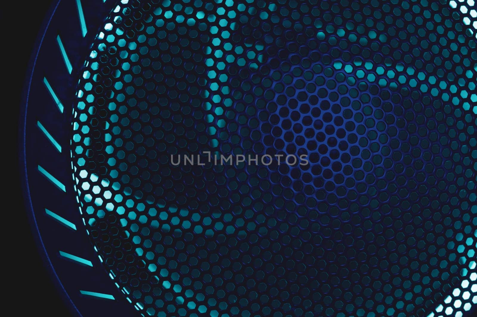 Colorful light of computer fan shines through the holes of protective grid. illumination glows in the dark. abstract futuristic background. led lighting of gaming pc