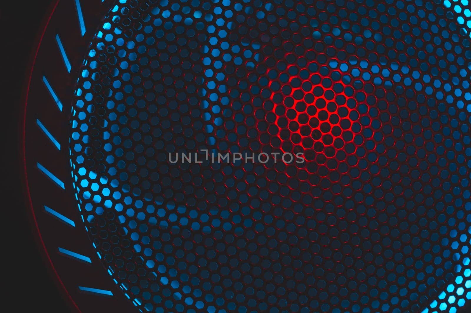 Colorful light of computer fan shines through the holes of protective grid. illumination glows in the dark. abstract futuristic background. led lighting of gaming pc