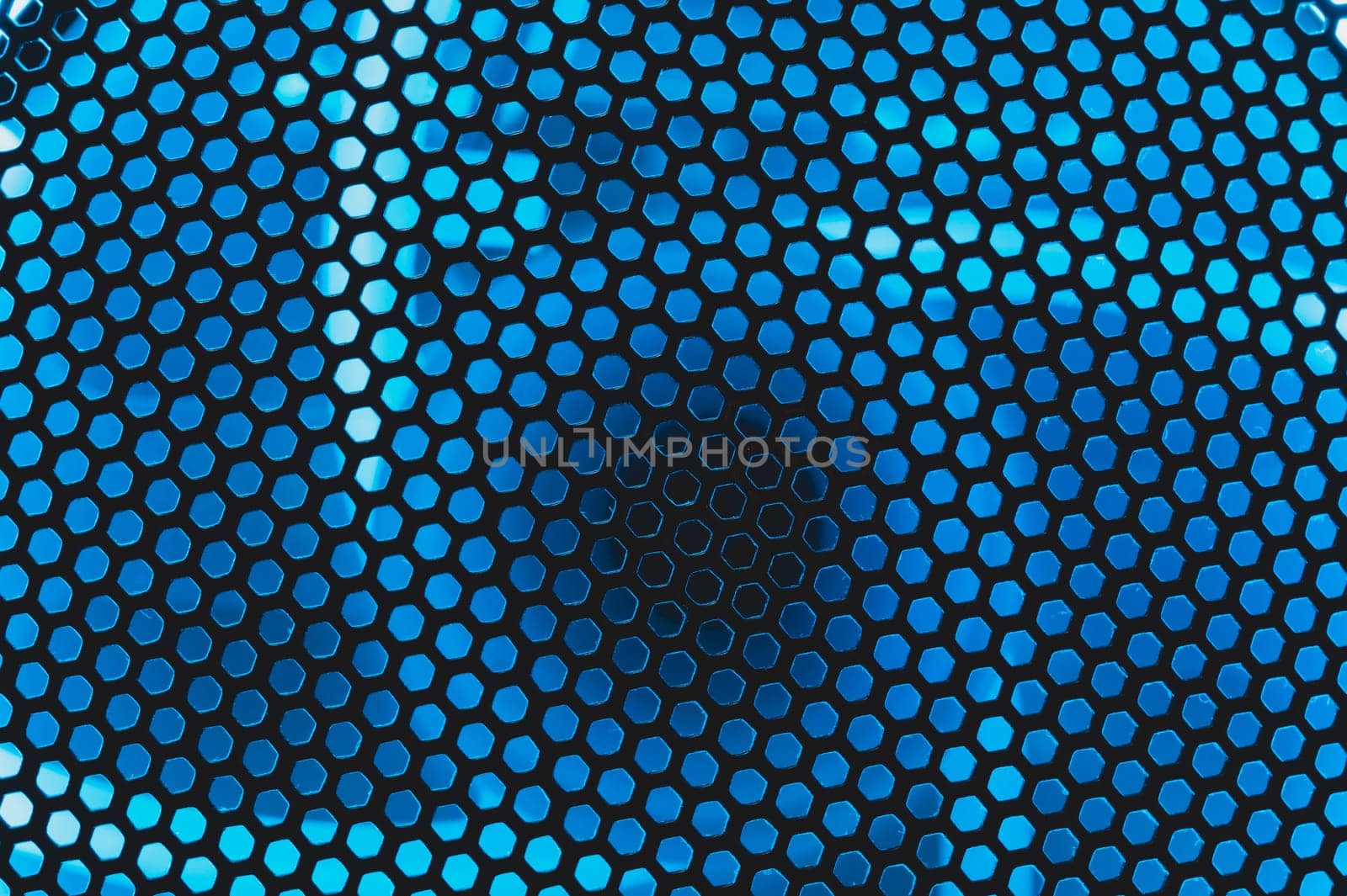 Blue light shines through the ventilation grid holes of computer air cooling system. abstract background