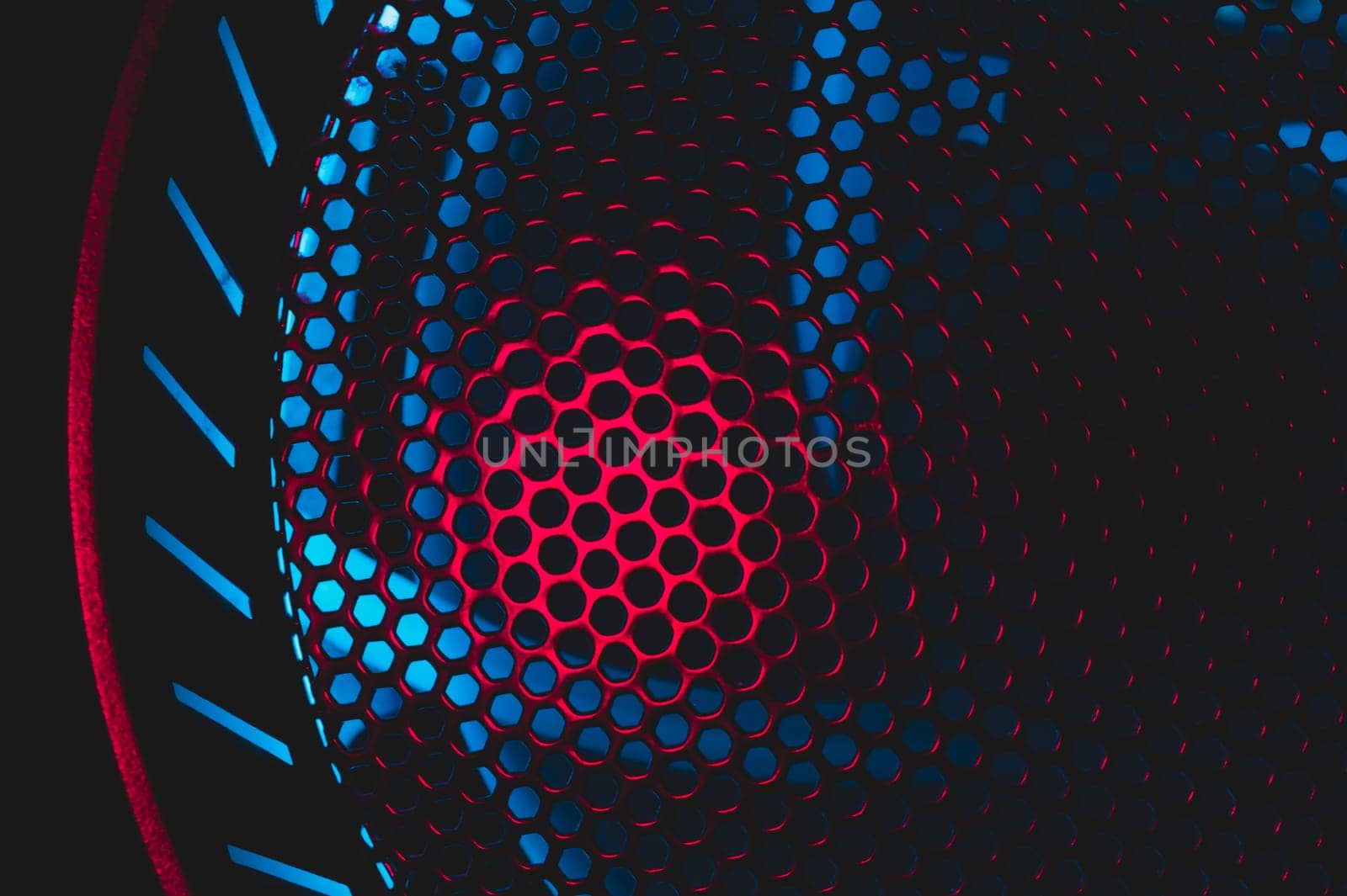 Colorful light of computer fan shines through the holes of protective grid. illumination glows in the dark. abstract futuristic background. led lighting of gaming pc