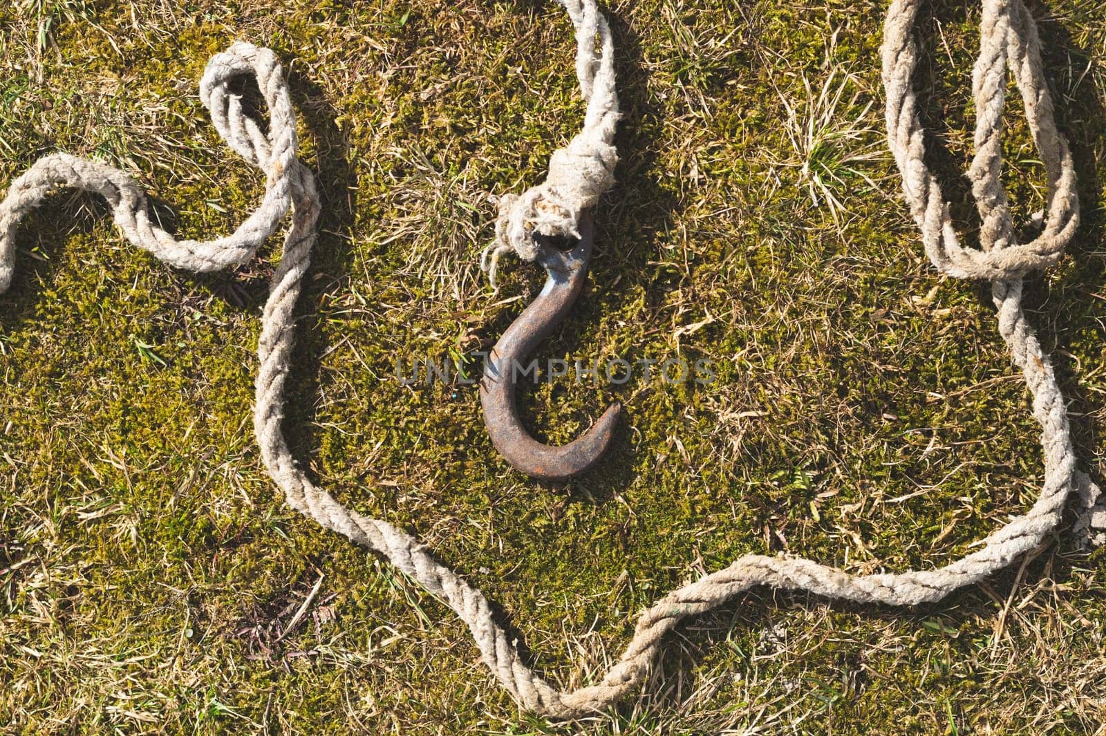 Rusty metal hook with rope lies on the green grass. marine equipment