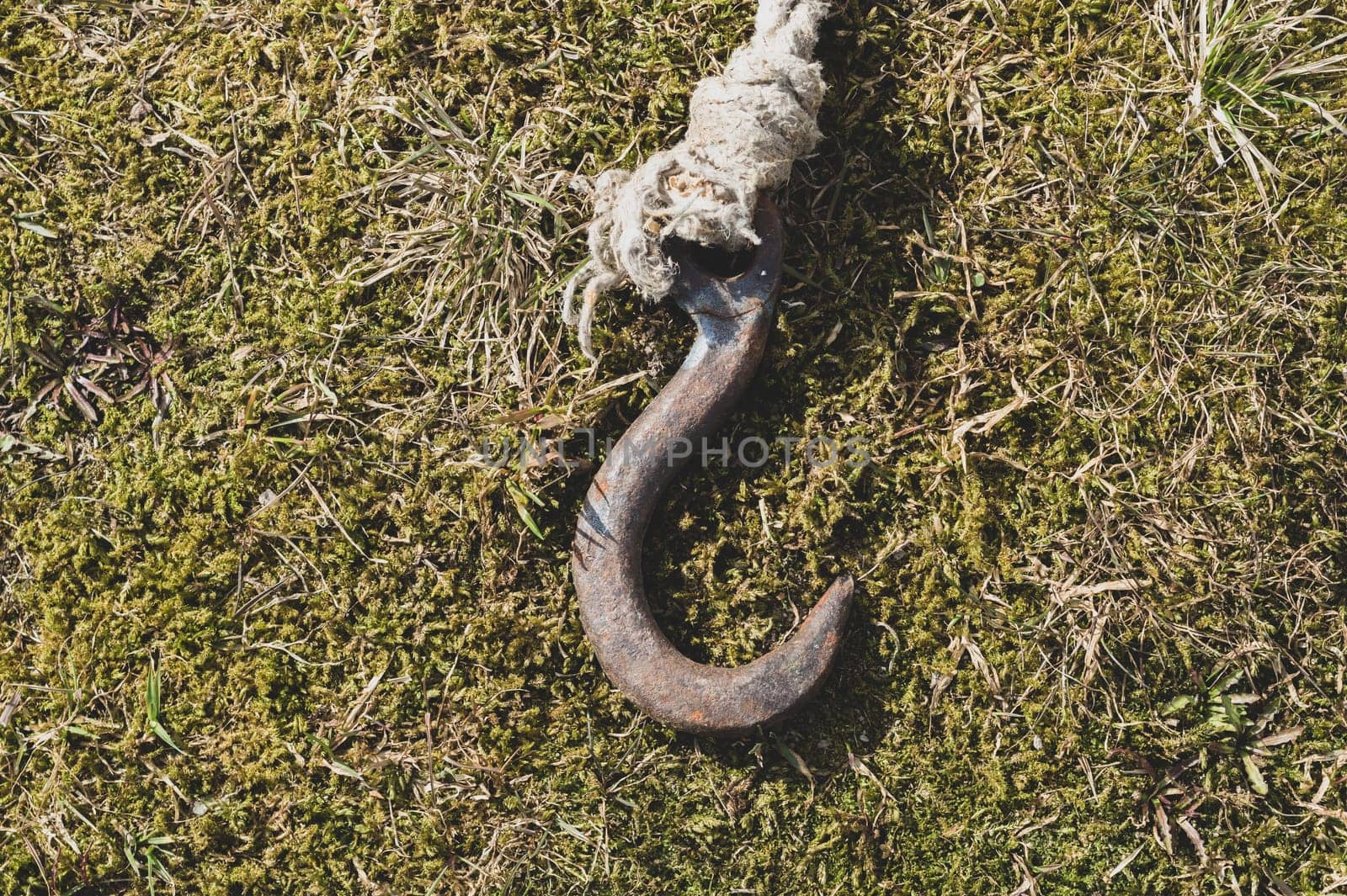 Rusty metal hook with rope lies on the green grass. marine equipment