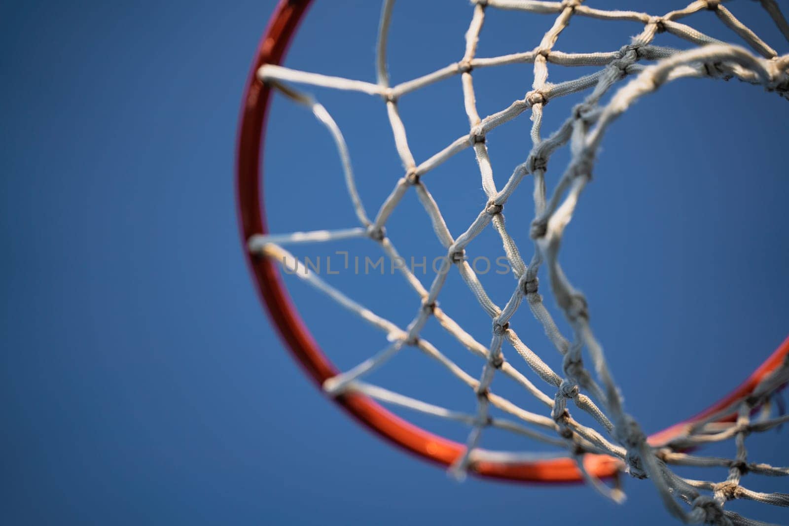 closeup of outdoor basketball basket net of white rope view from underneath against a blue sky with copyspace