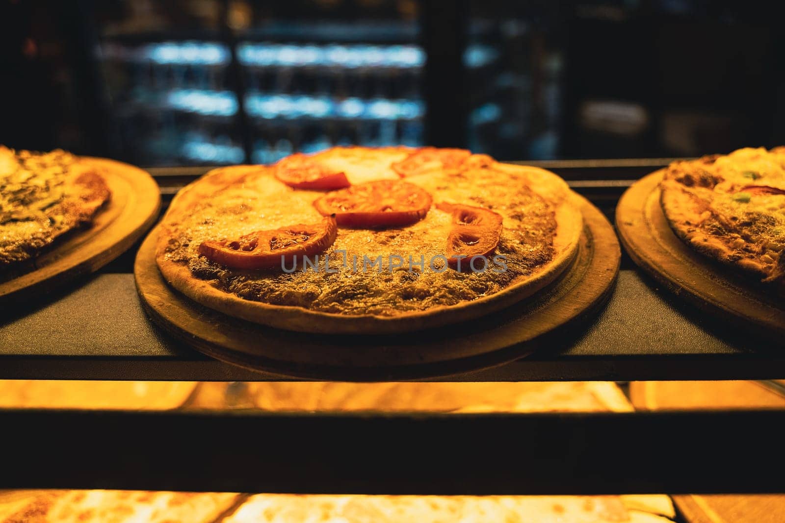 perspective view closeup of different kinds of pizza on wooden plates on the shelves of street food shop window