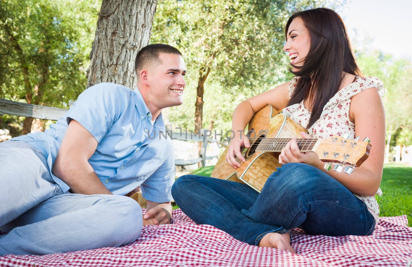 Young Adult Girl Playing Guitar with Boyfriend In The Park.