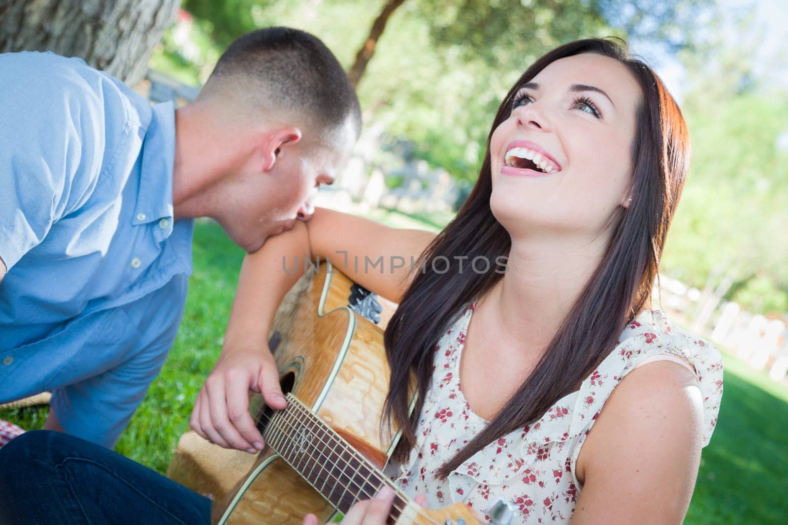Young Adult Girl Playing Guitar with Boyfriend In The Park.
