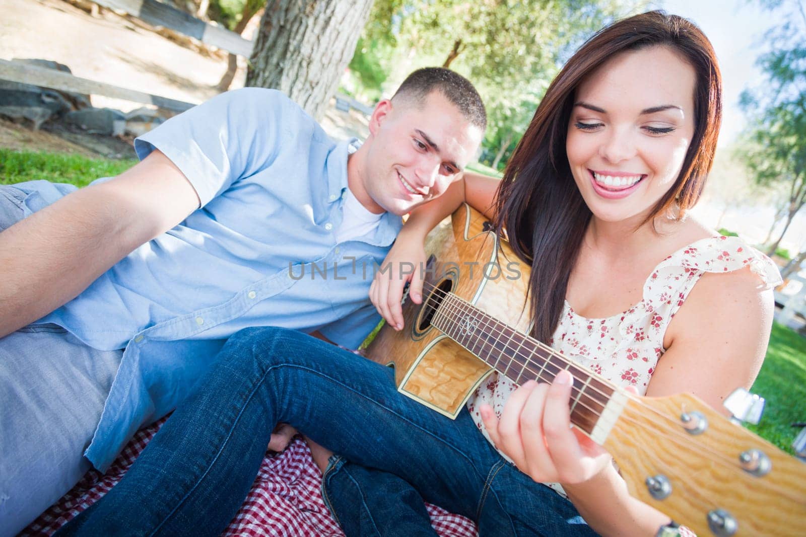 Young Adult Girl Playing Guitar with Boyfriend In The Park.