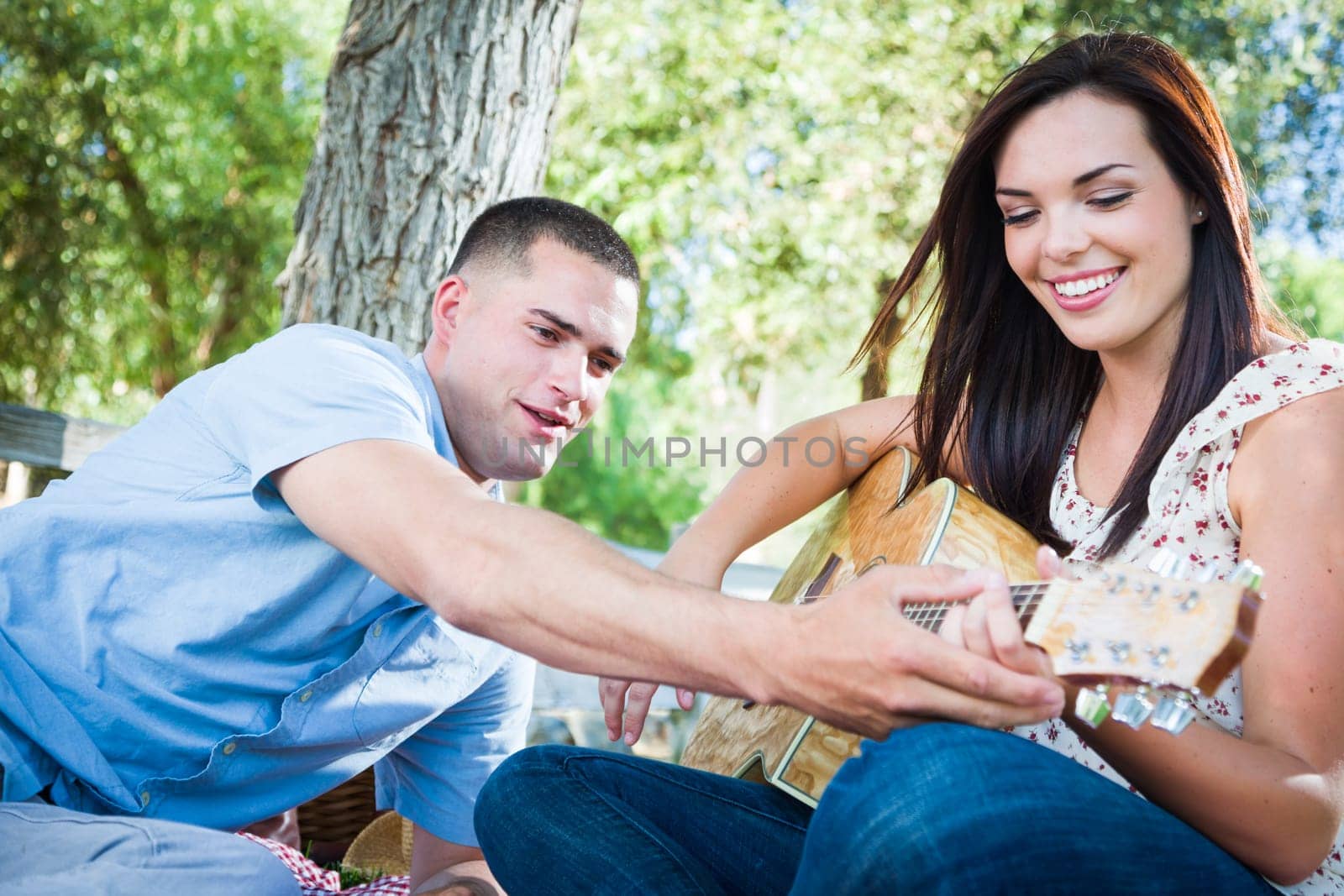 Young Adult Man Teaching Girlfriend How To Play The Guitar Outside in the Park.