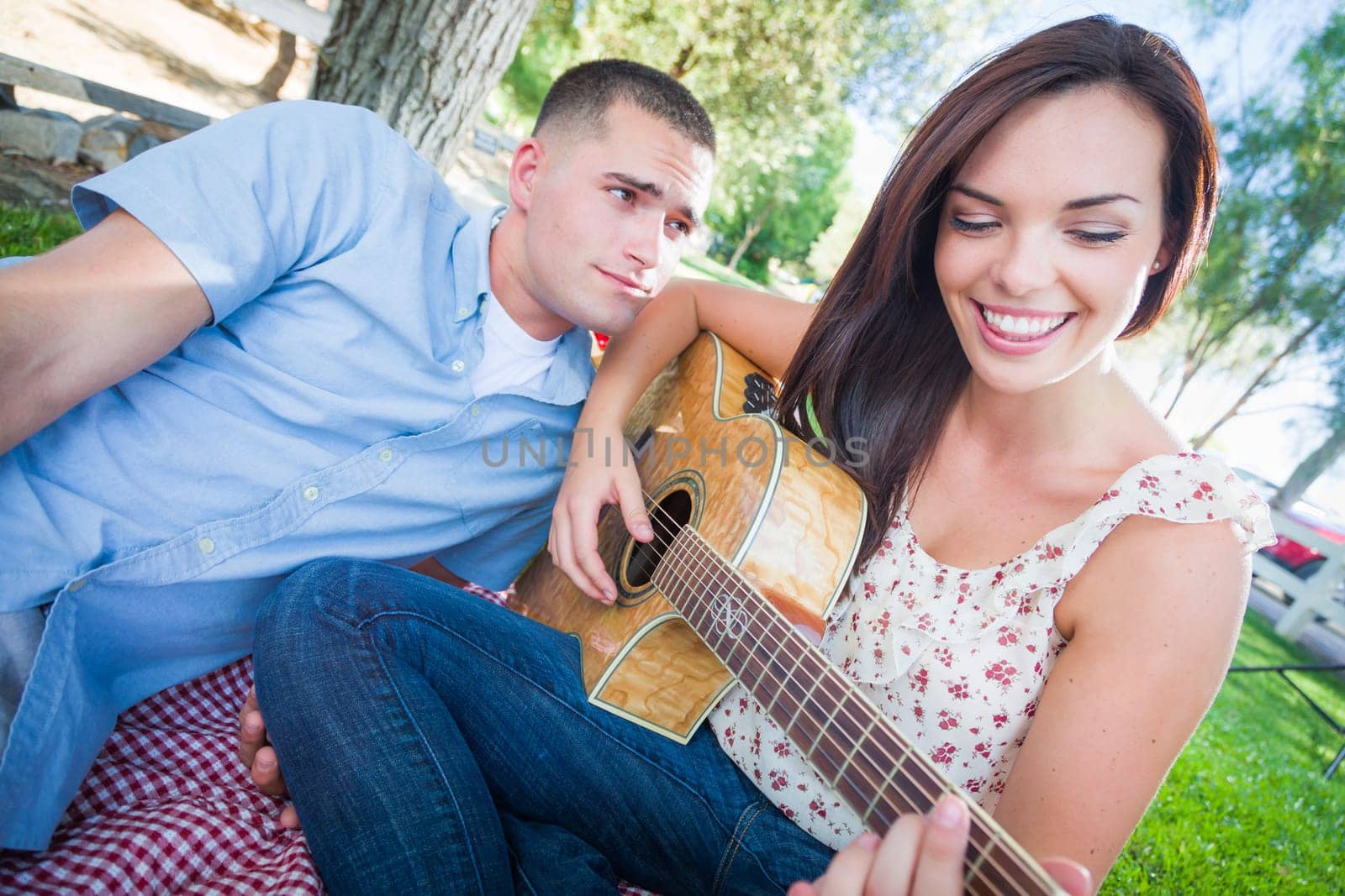 Young Adult Girl Playing Guitar with Boyfriend In The Park.