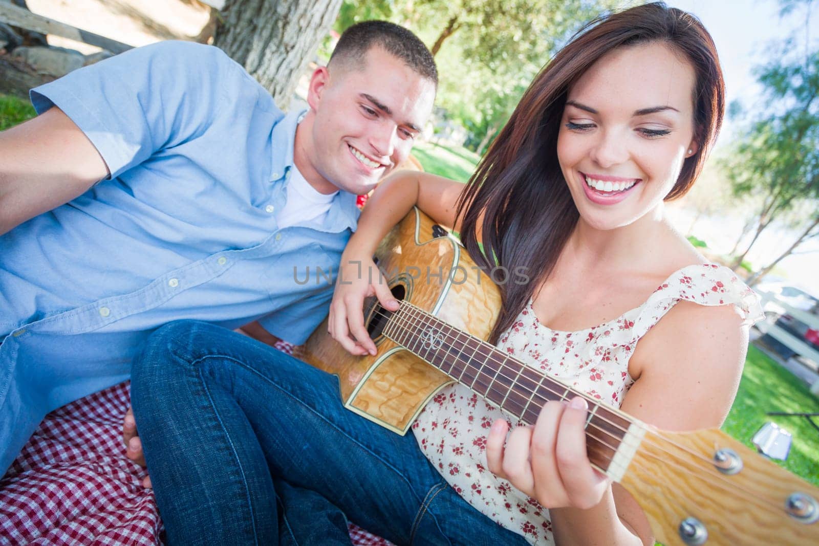 Young Adult Girl Playing Guitar with Boyfriend In The Park.